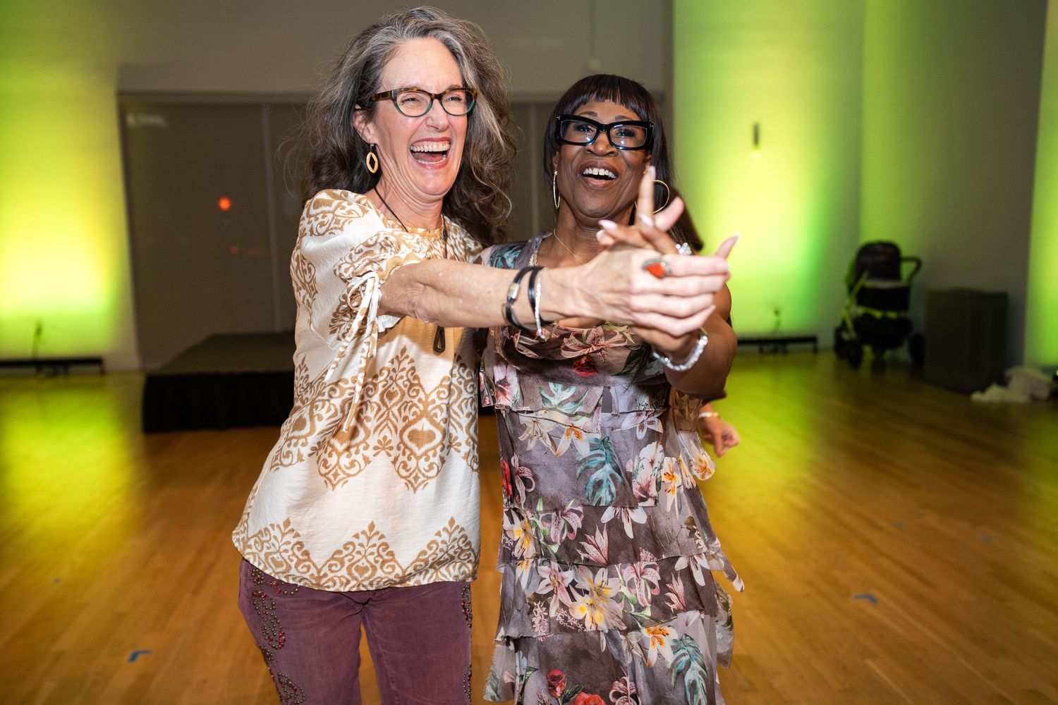Two dancers share a joyful moment on a wooden dance floor with green ambient lighting.