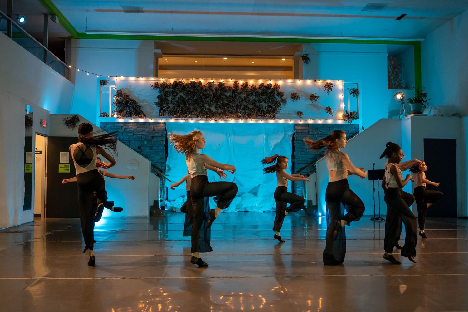 Energetic dancers performing hip-hop choreography on a stage with blue lighting and marquee backdrop.