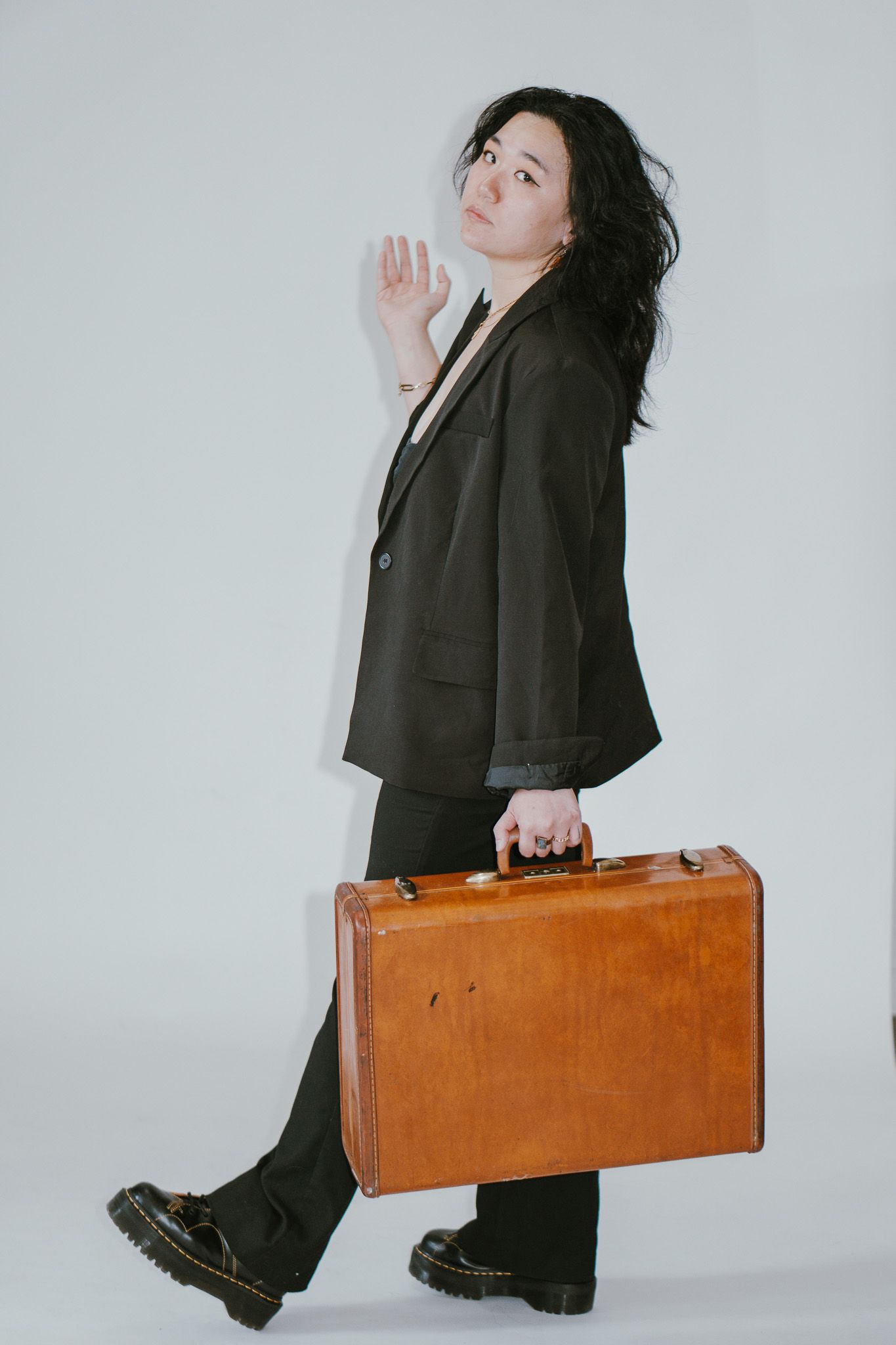 Stylized portrait series with black suit and brown suitcase against minimal background.
