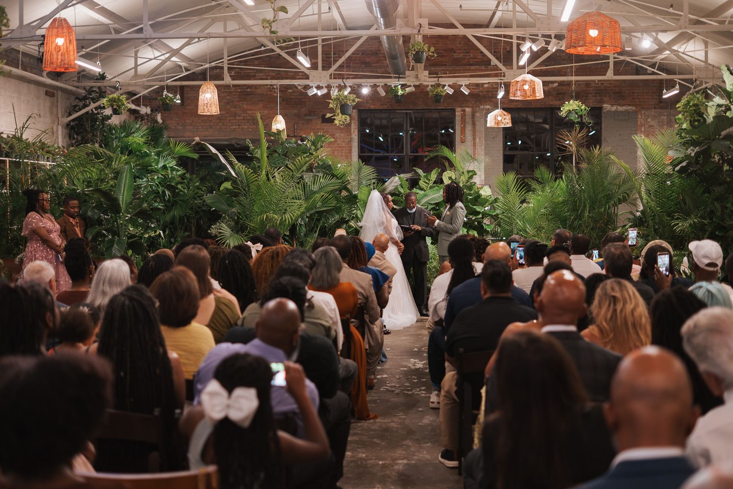 Elegant indoor wedding ceremony surrounded by lush tropical plants with guests seated in rows facing the altar.