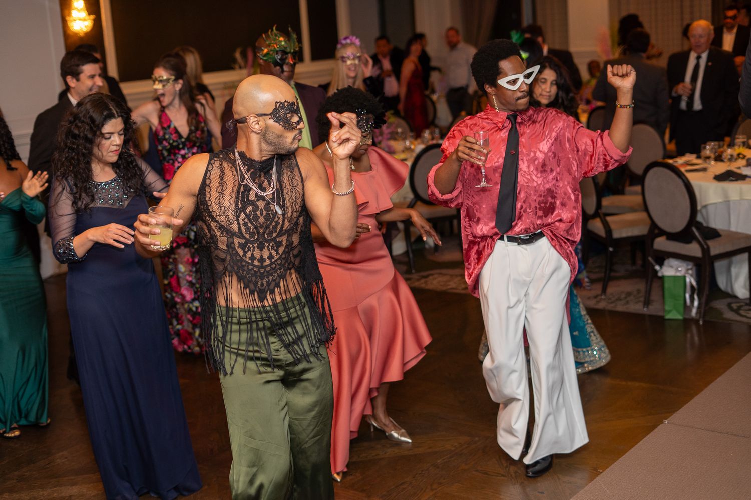 Guests in masquerade masks and festive attire dancing at an elegant masquerade ball.