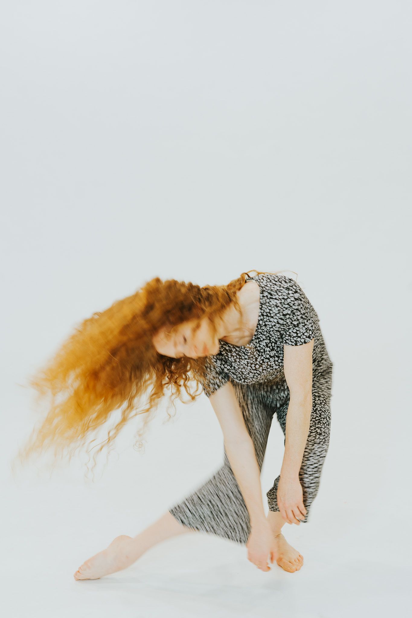 Artistic dance sequence showing flowing red hair and grey patterned dress against light backdrop.