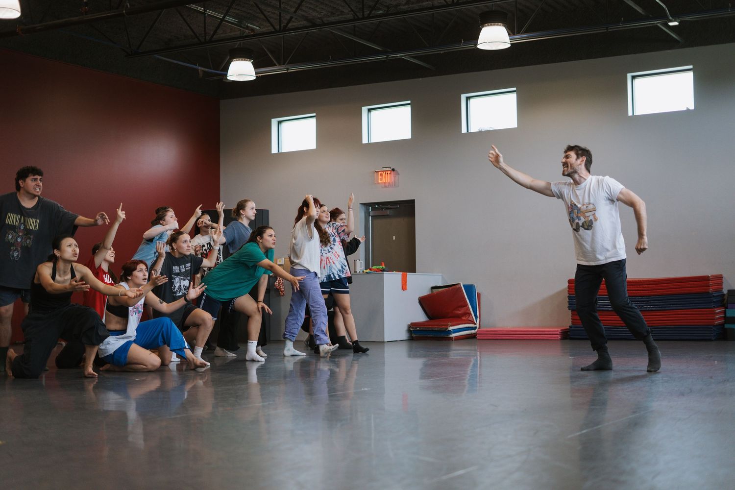 Dance instructor leads energetic group movement class in modern studio with high ceilings and large windows.