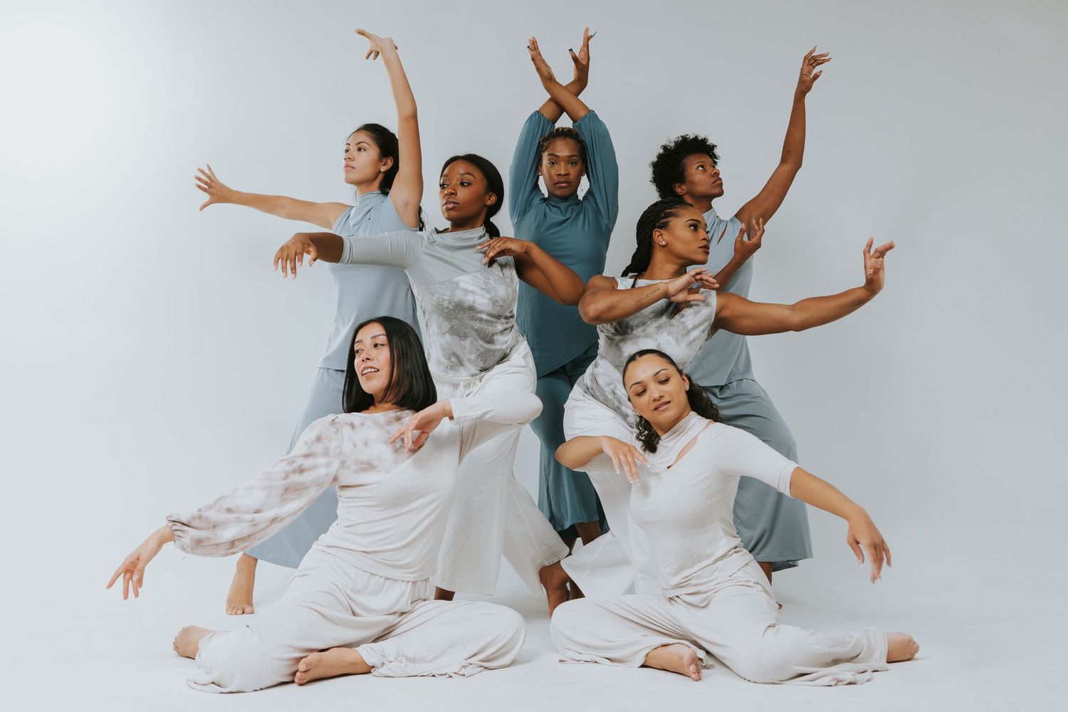 Seven diverse dancers pose dynamically in white and blue outfits against a white background.