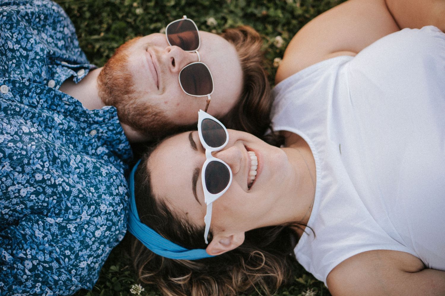 Couple lying down wearing matching sunglasses and smiling during spring photo session.
