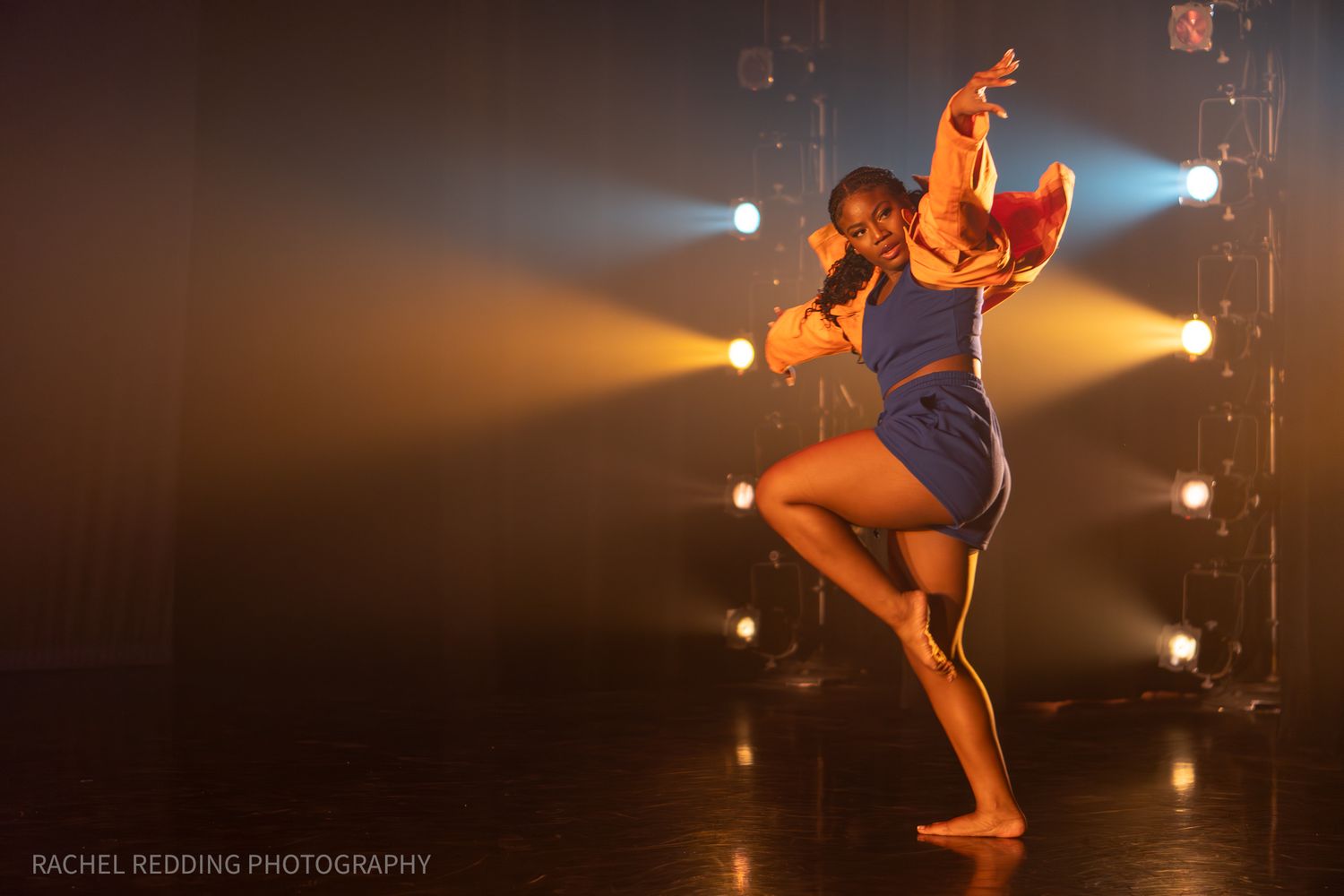 A contemporary dance performance with dramatic lighting shows a dancer leaping gracefully on a dark stage.