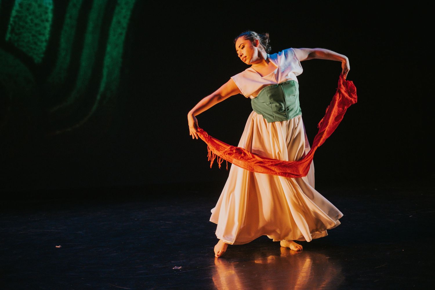 Dancers in flowing dresses perform an expressive choreography under stage lights.