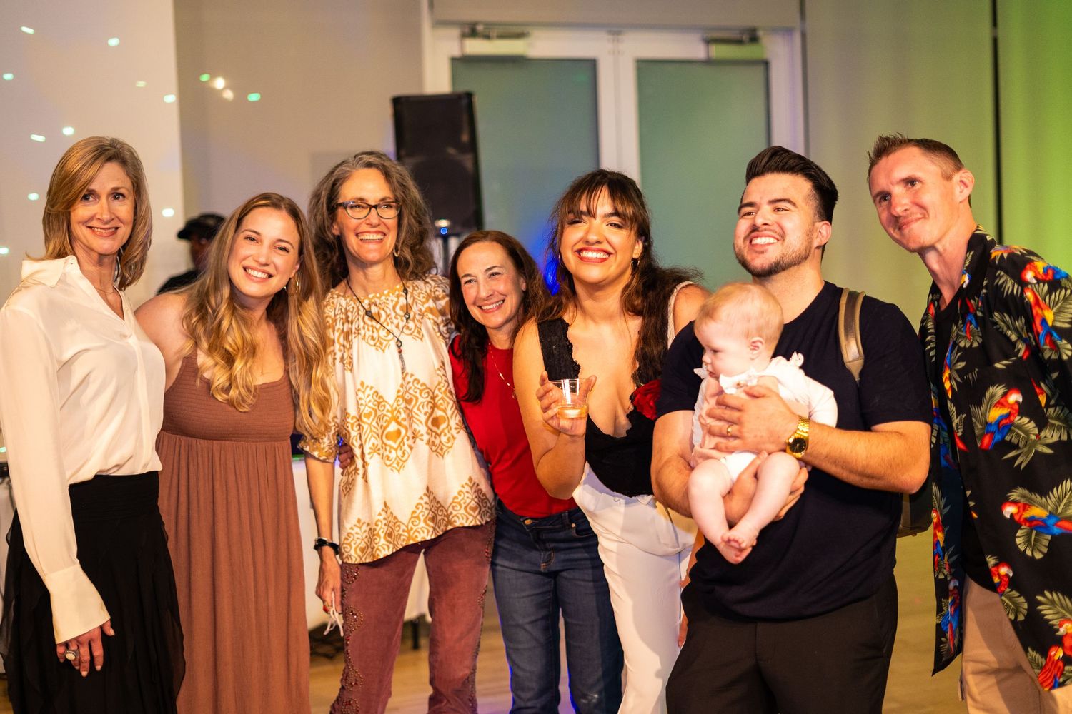 Group of friends gather for a celebratory photo at a social event with green lighting.