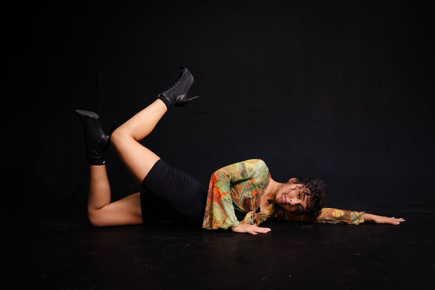 Artistic floor pose in dim lighting with patterned fabric styling.