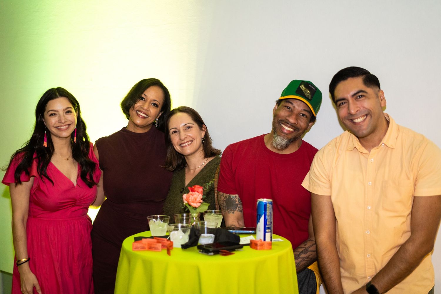 Five friends gather around a bright yellow table at a social event.
