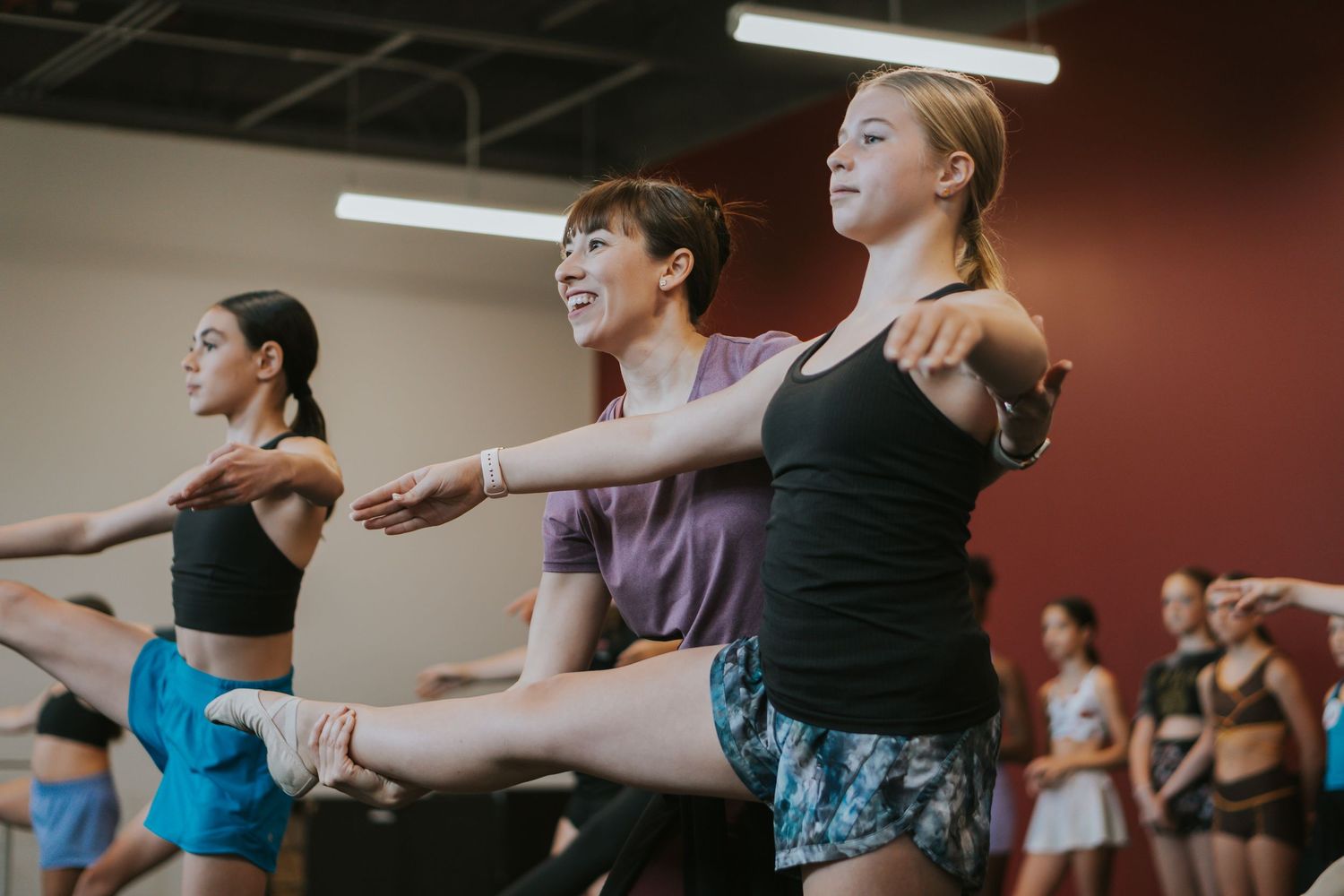 Dancers stretching their arms in synchronization during a group dance class with mirrored walls.