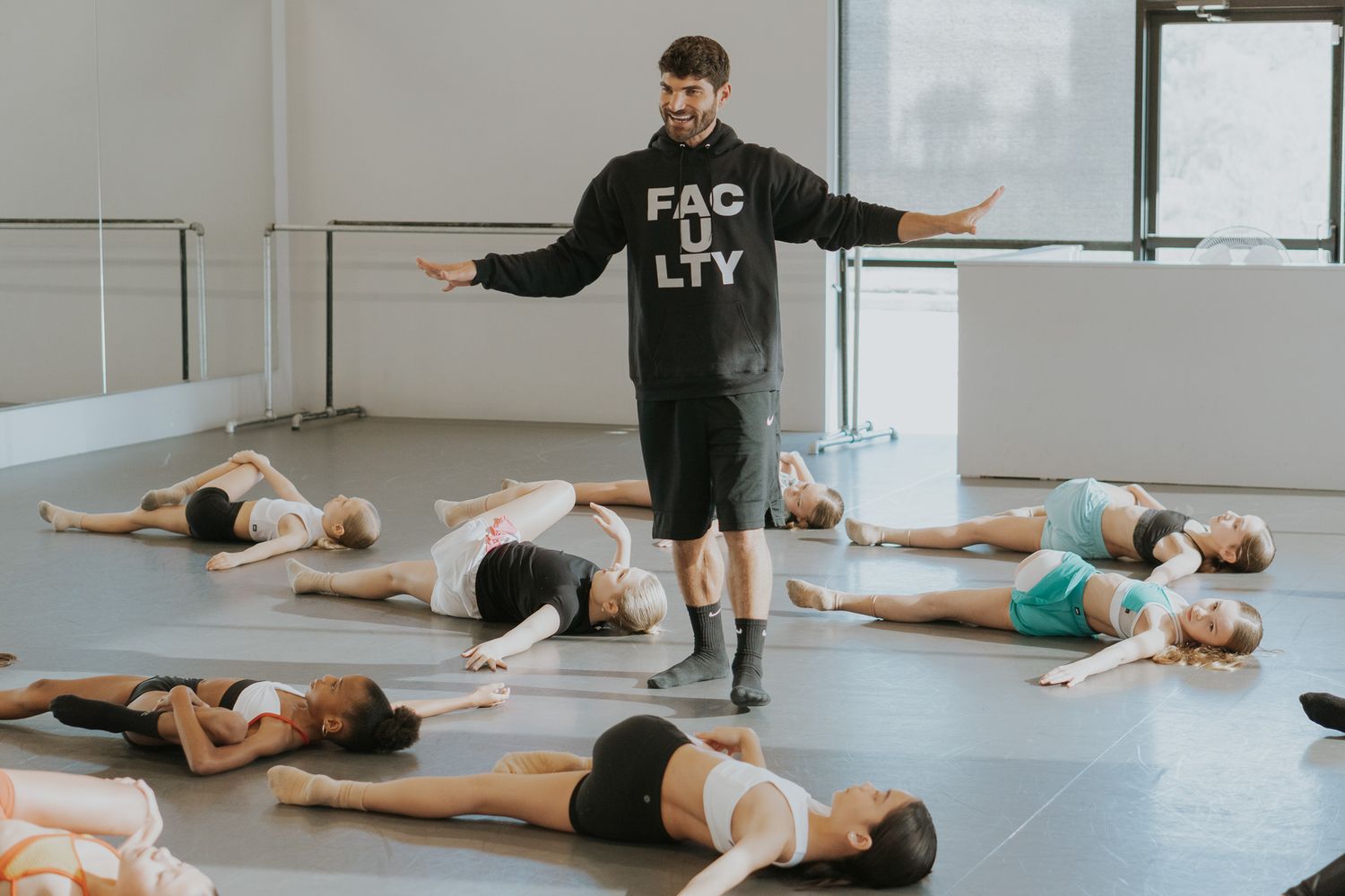 Dance instructor leading floor exercises as students lie on mats in a studio.
