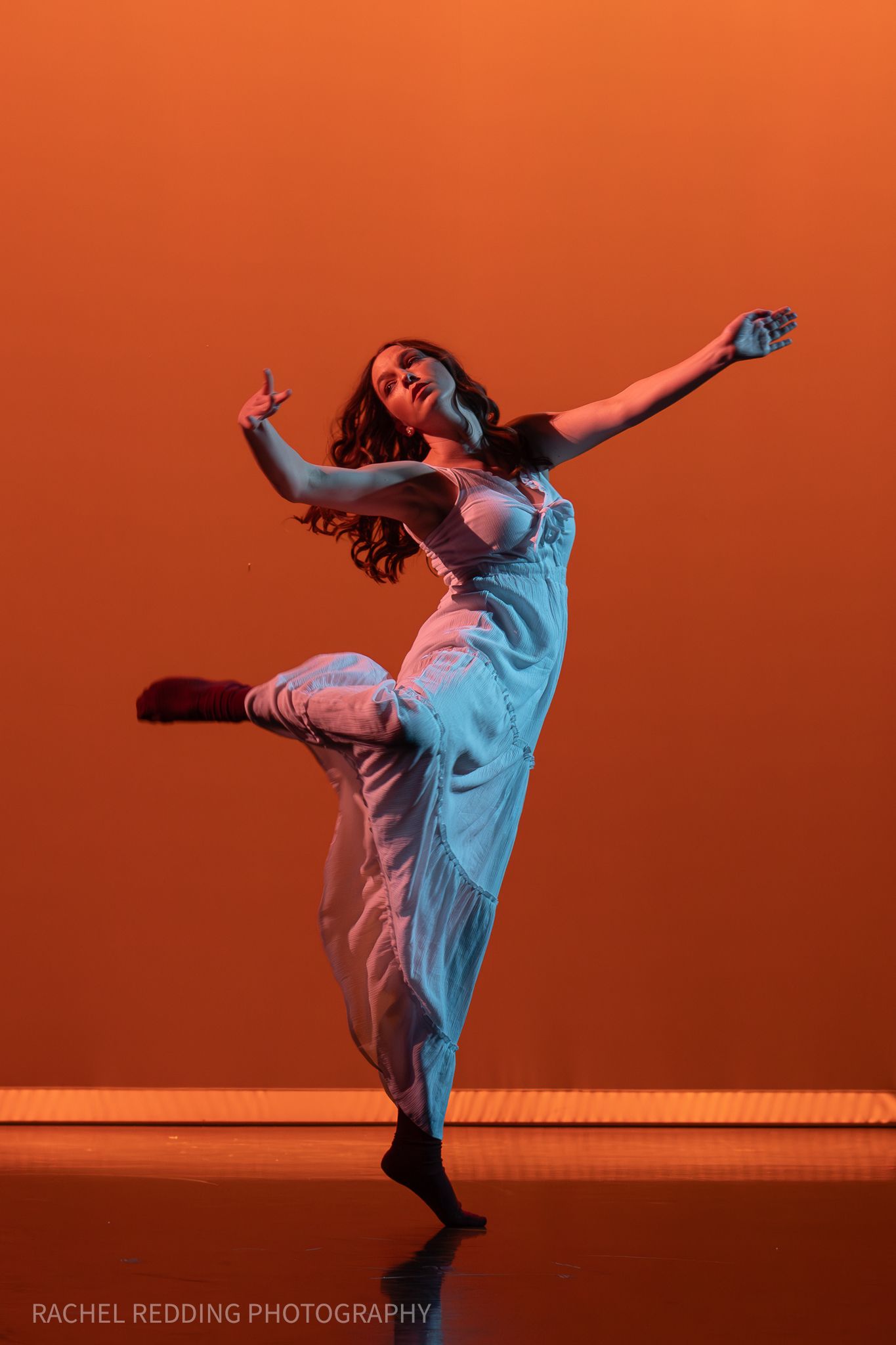 Modern dancer performs expressive moves against an orange backdrop, creating a dramatic silhouette in white attire.