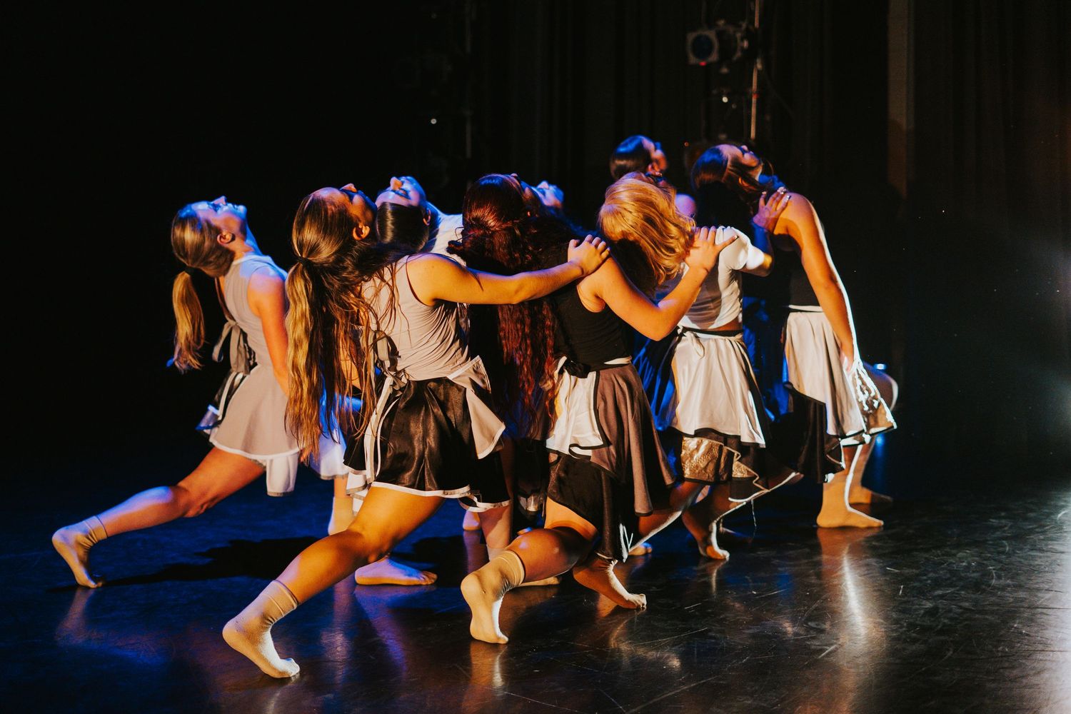 A line of dancers executes coordinated movements in matching costumes on stage.