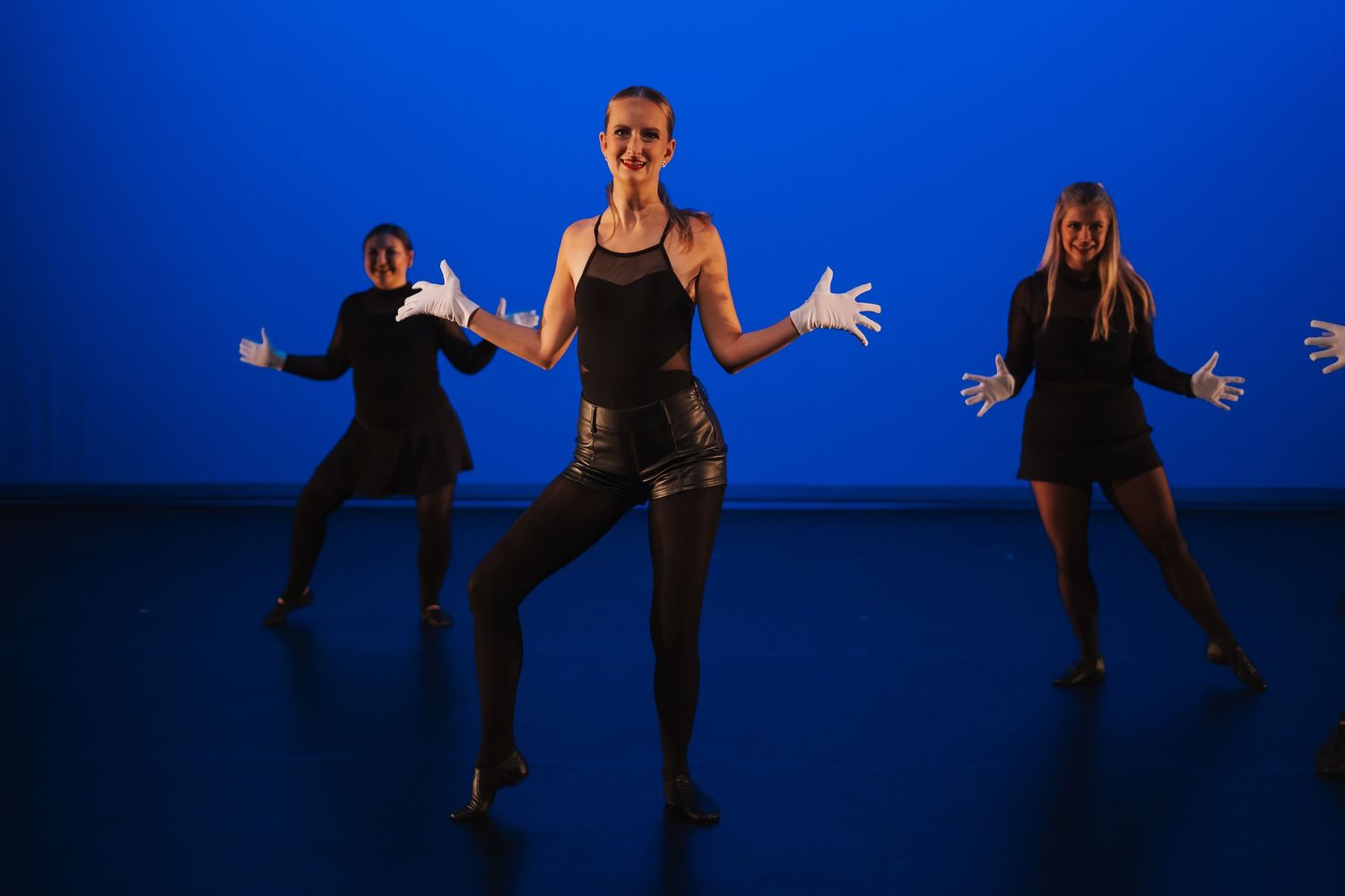 Six dance silhouettes perform a dynamic choreographed sequence against a vibrant blue background.