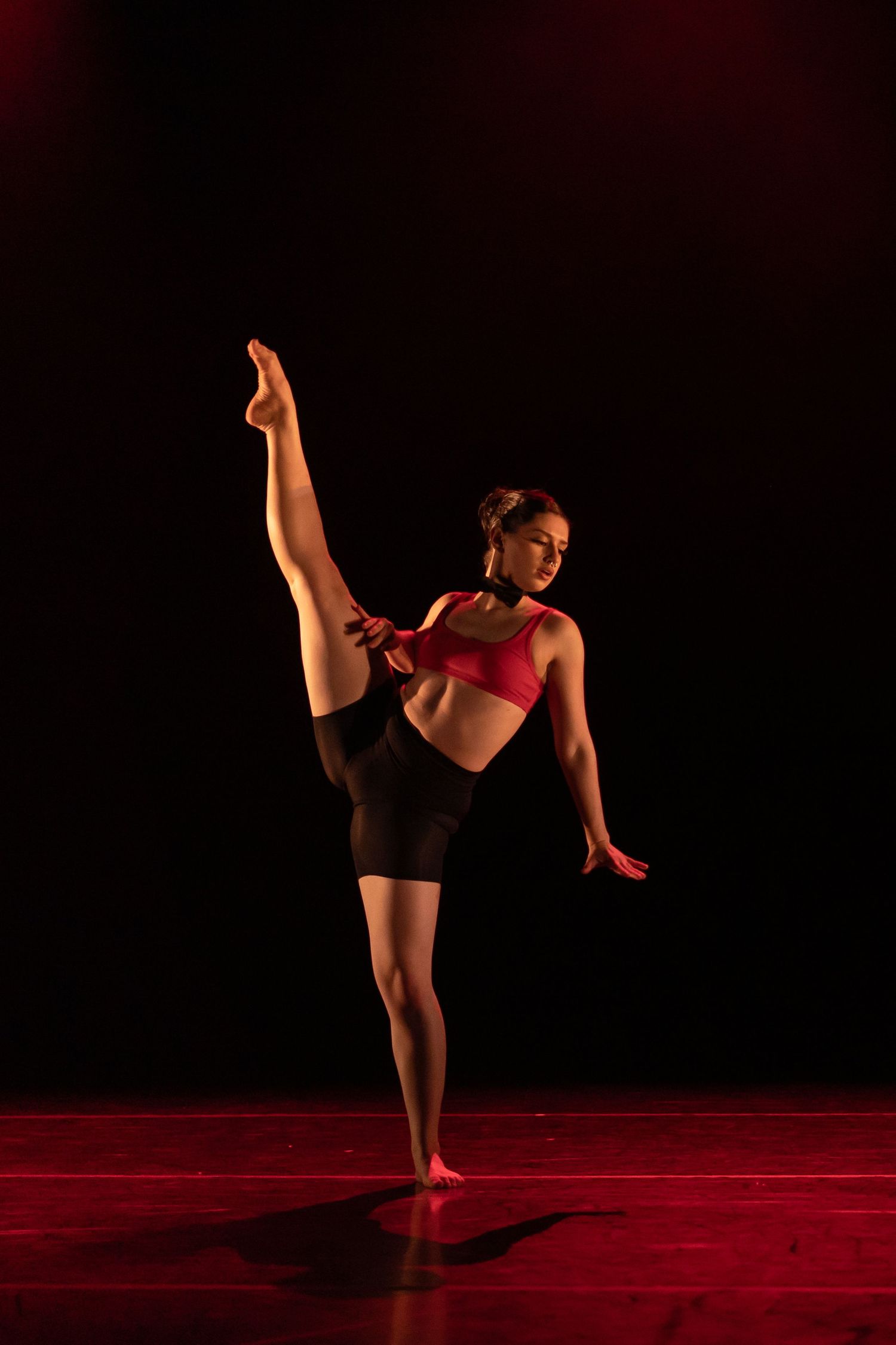 Solo dancer performs athletic movements under red lighting on stage.