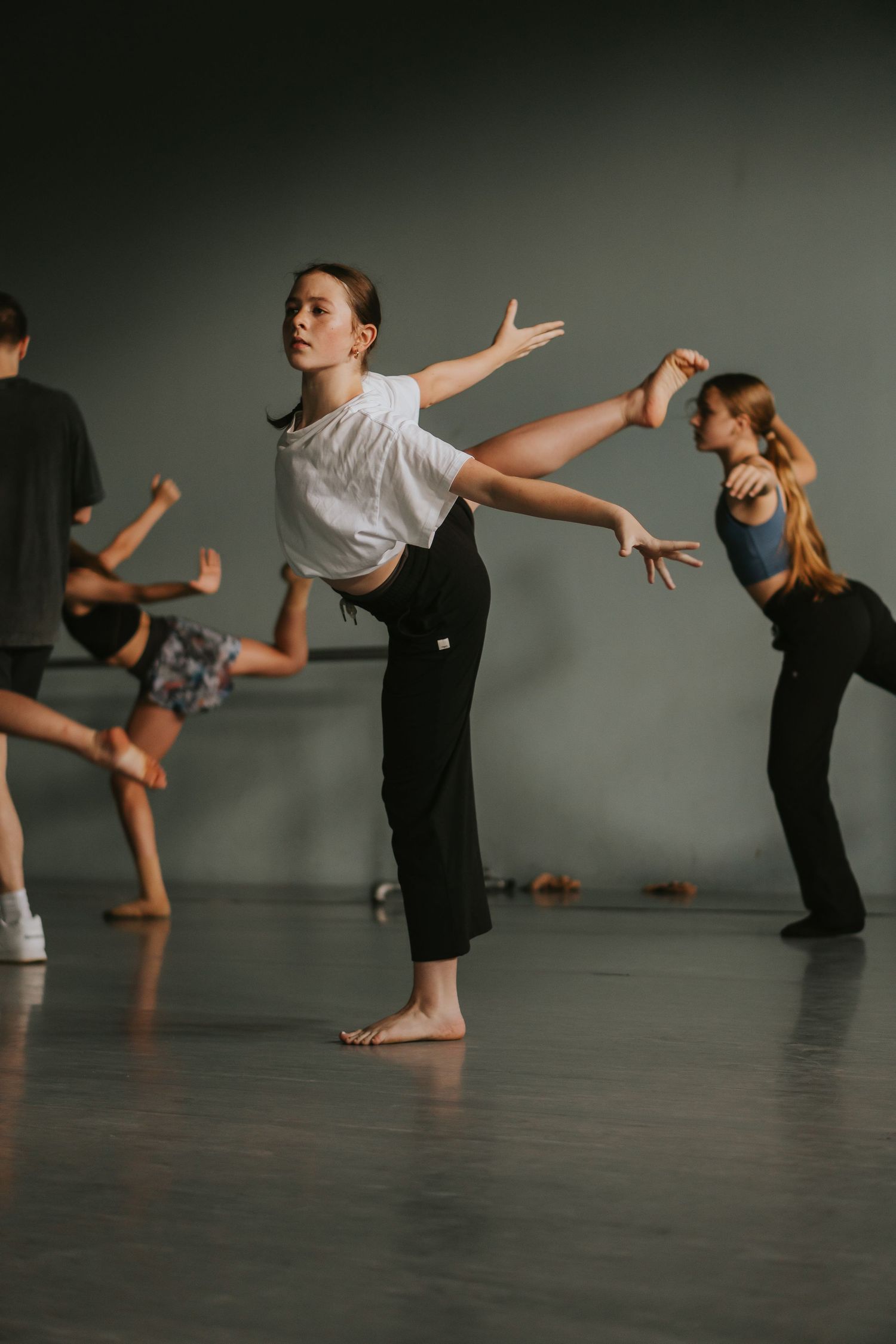 Dancers performing graceful arm movements in silhouette against a dark studio backdrop.