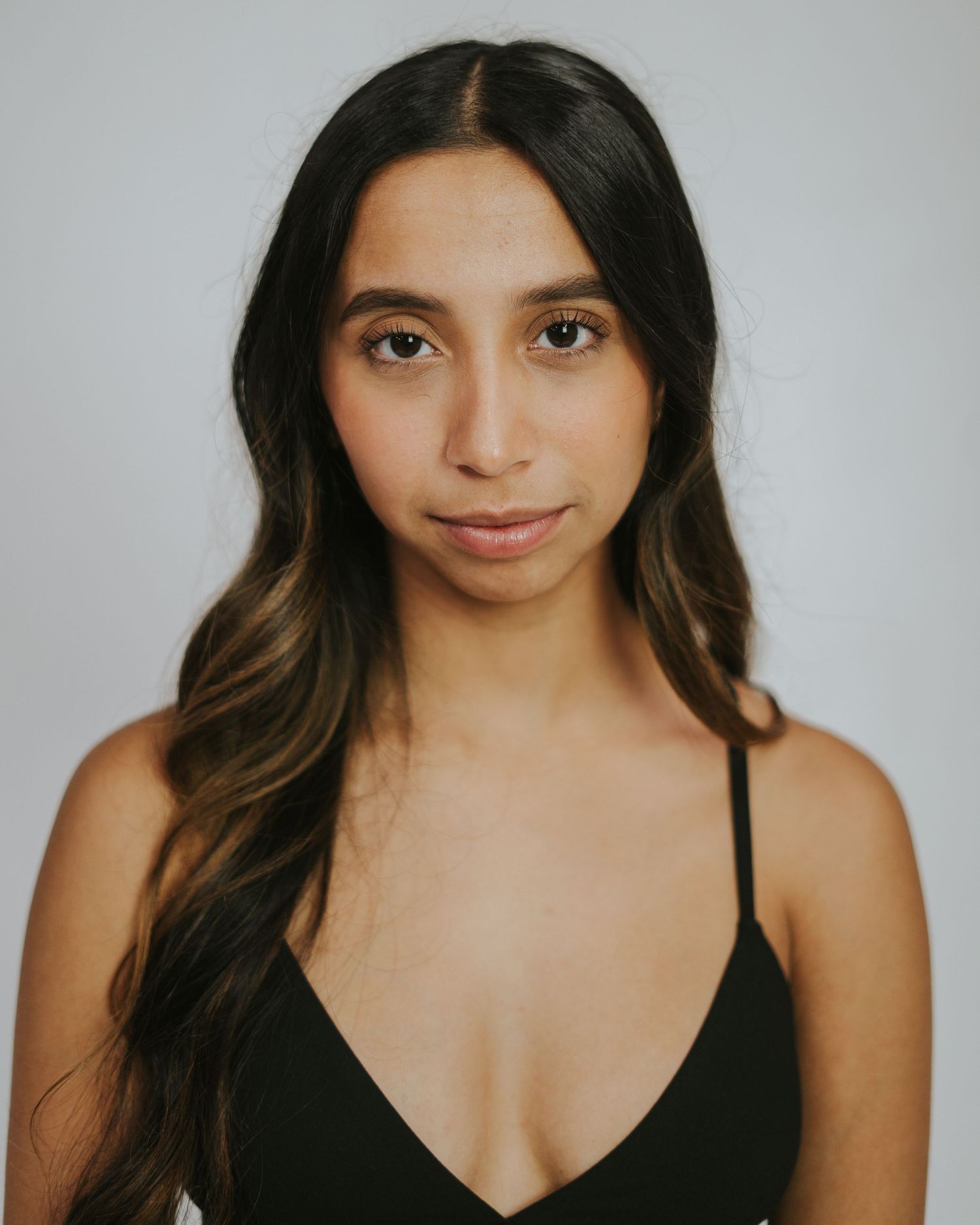 Portrait of person with long dark hair and highlights wearing a black top against light background.
