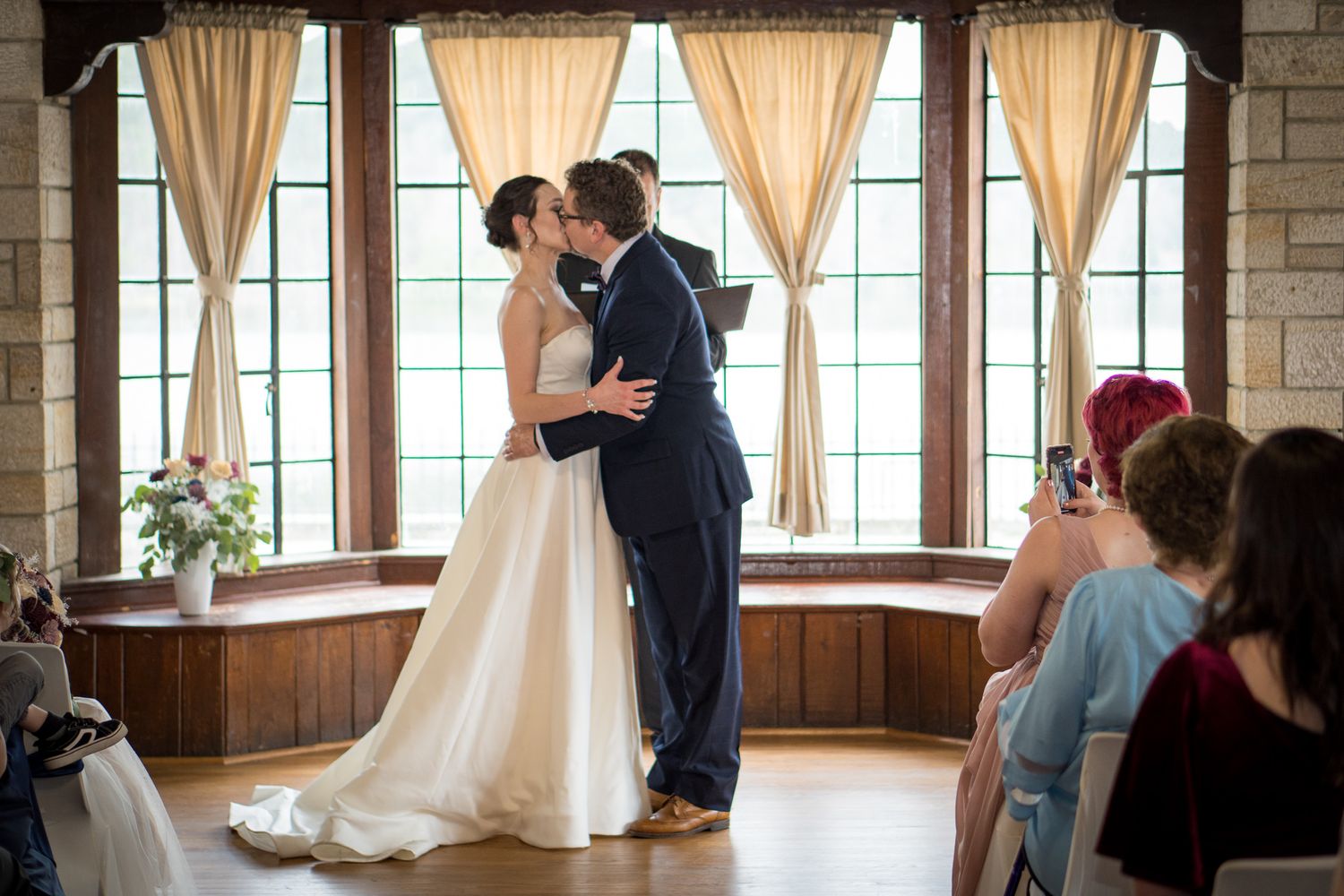 Wedding couple dancing in an elegant venue with large windows and cream curtains.