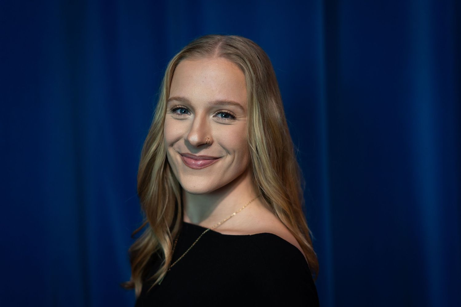 Professional headshot of someone in black top against blue backdrop.