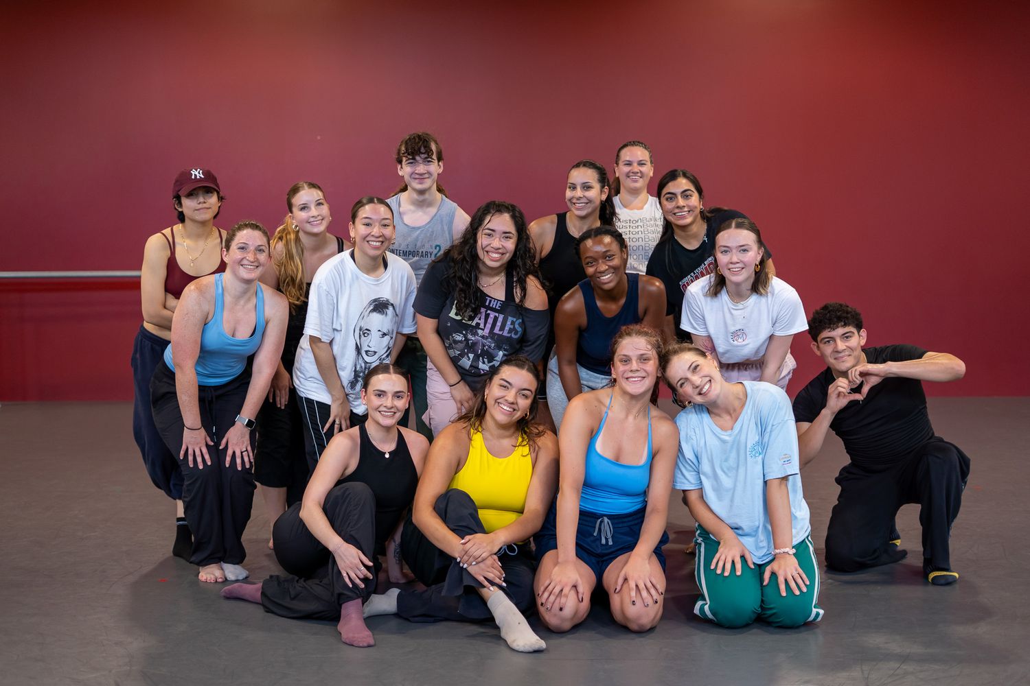 A diverse group of teenage dancers poses together in a red-walled dance studio, smiling and holding basketballs.