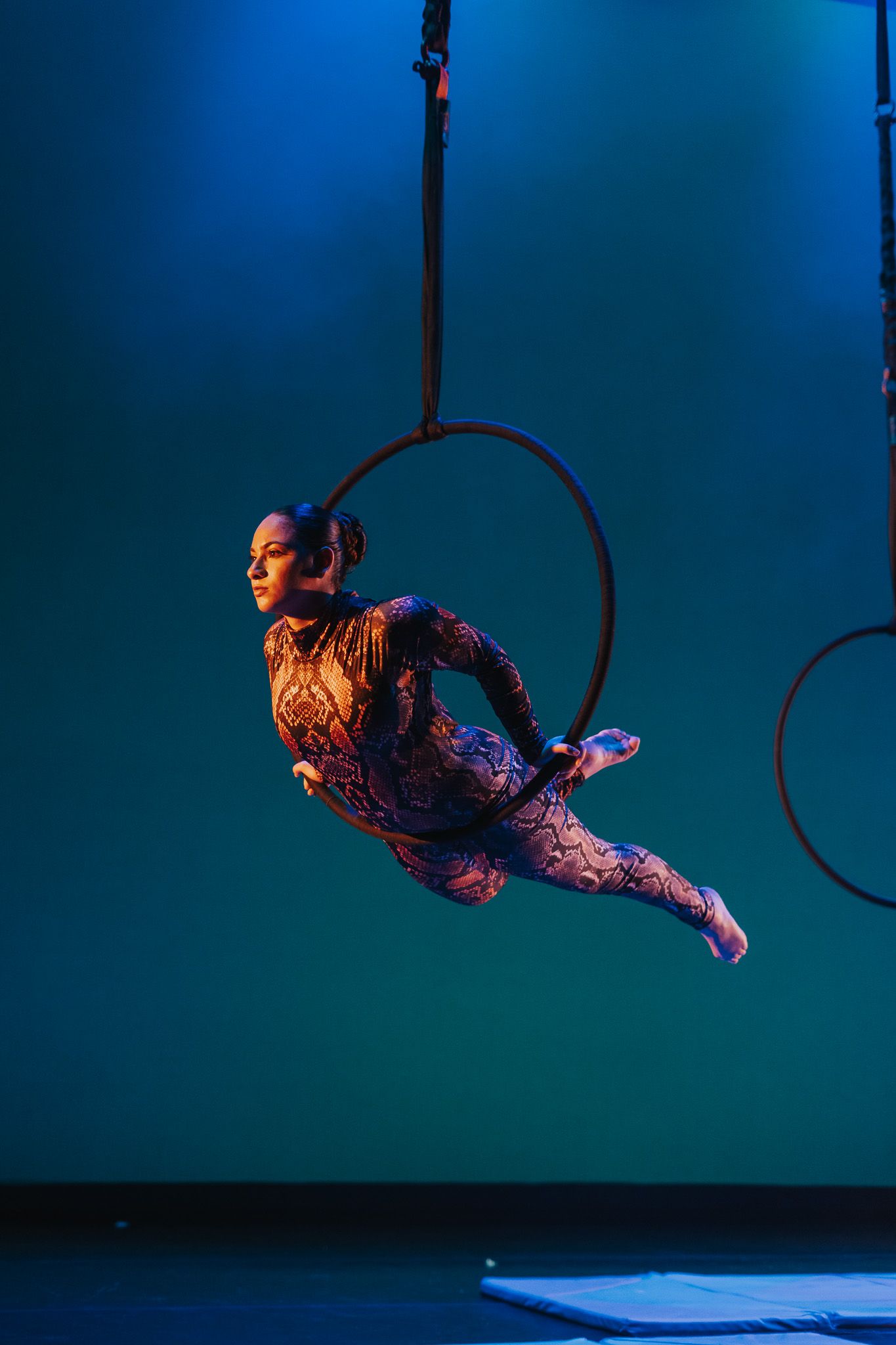 An aerial performer in a colorful costume gracefully soars through the air on a suspended hoop.