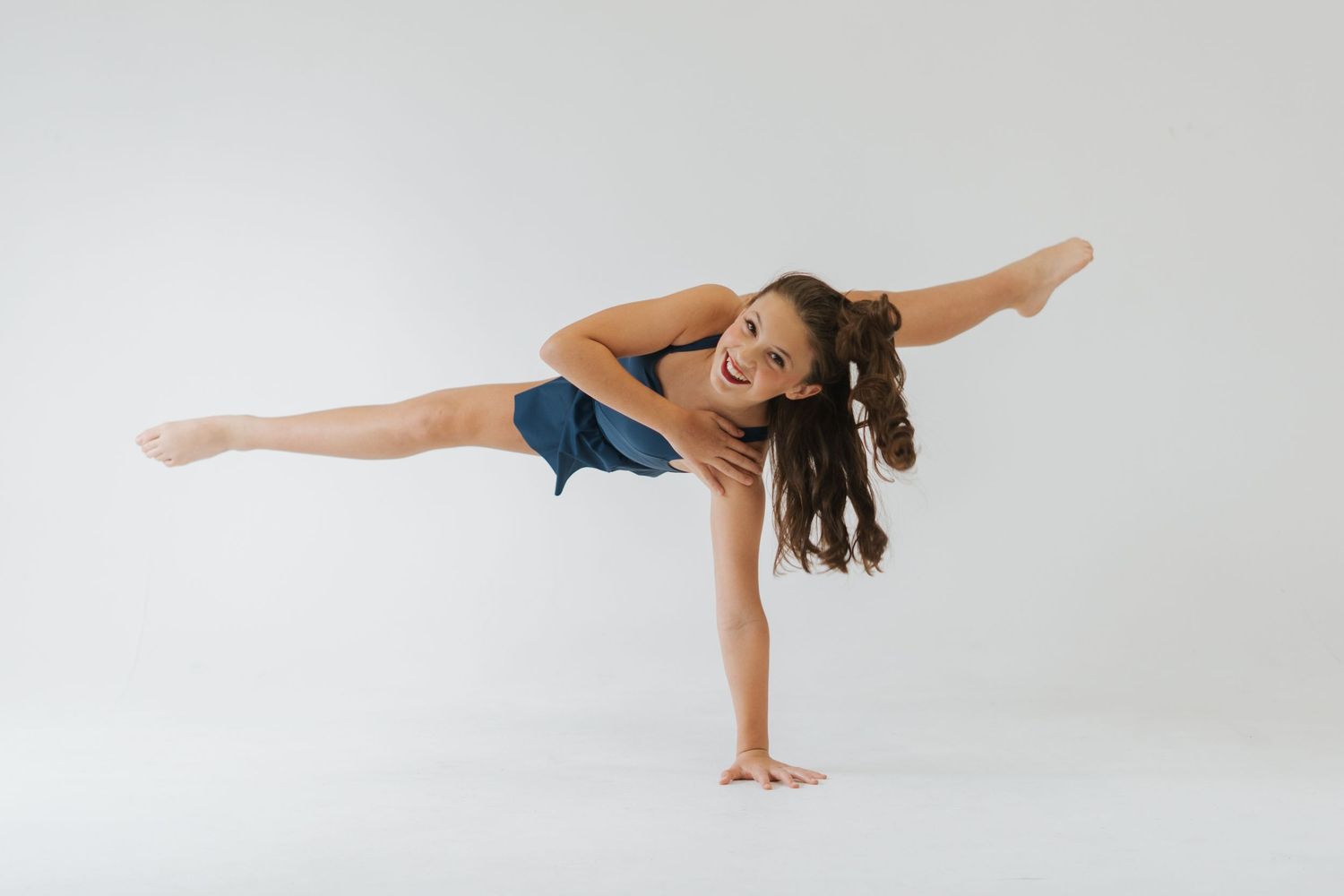 A dancer performs a dynamic balance pose with one leg extended while supporting weight on arms against white backdrop.