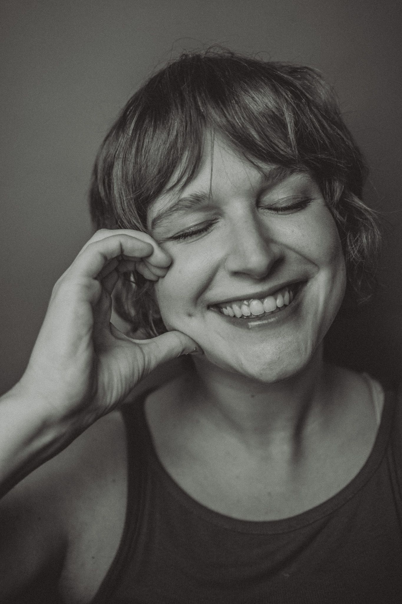 Black and white portrait of a smiling person with closed eyes in a candid moment of joy.