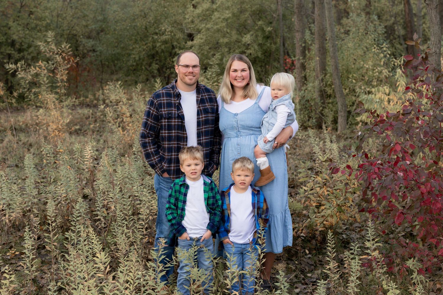 Family members wearing coordinated denim and plaid outfits pose together in an autumn forest setting.