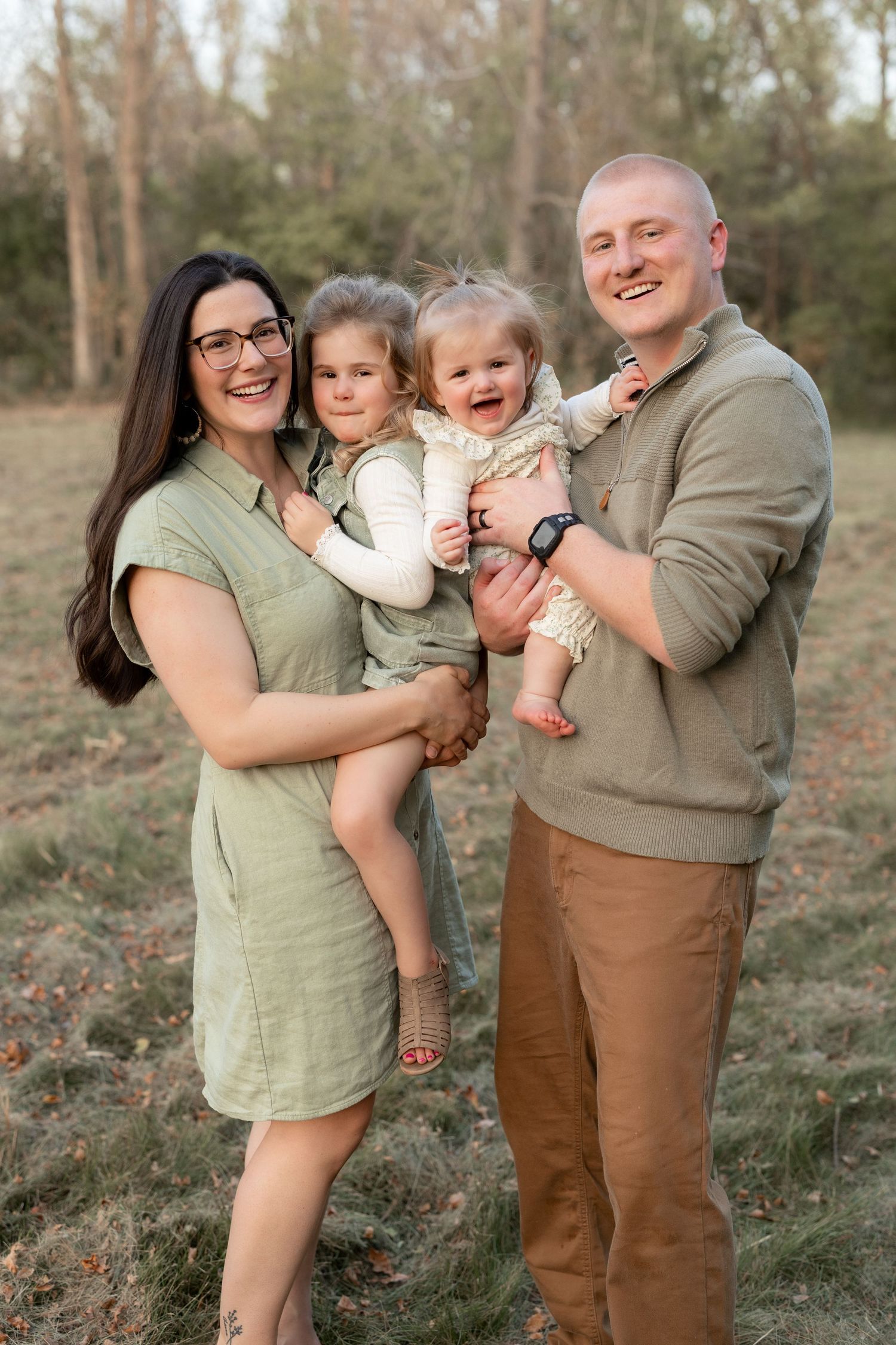 A family shares joyful moments together in a wooded outdoor setting wearing coordinated earth-tone outfits.