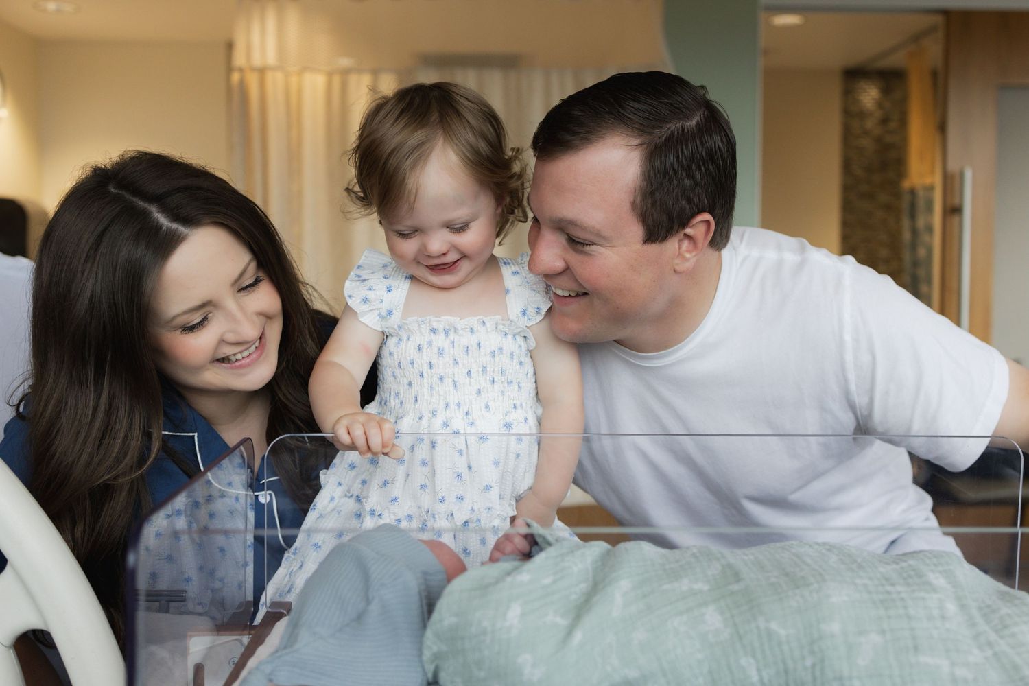 A family shares tender moments together while sitting on a couch in a bright living room setting.