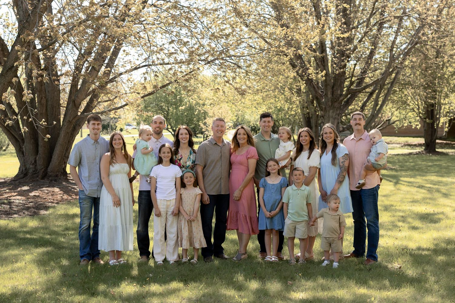 Large family group portrait outdoors under blooming trees on green lawn in spring.