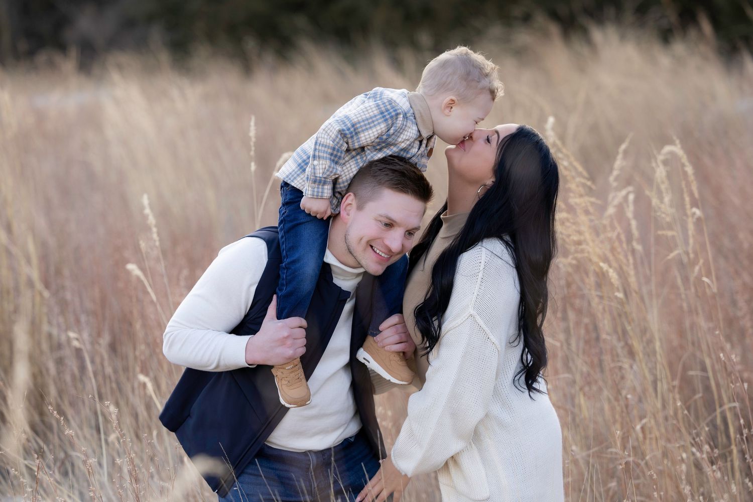 A romantic couple embraces in a golden field of tall grass at sunset.