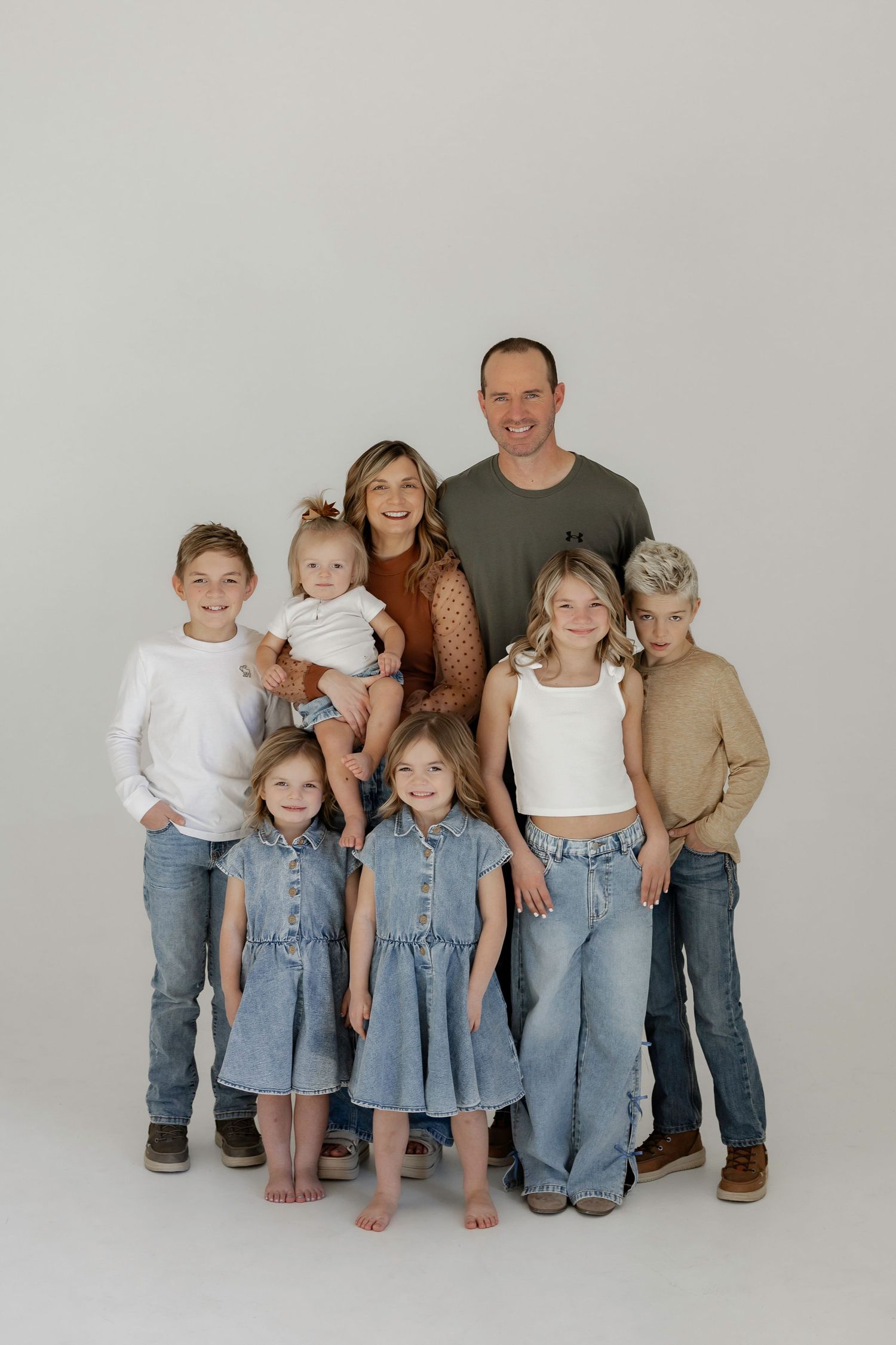 Family portrait of parents with six children in coordinating outfits, posing together against a white studio background.