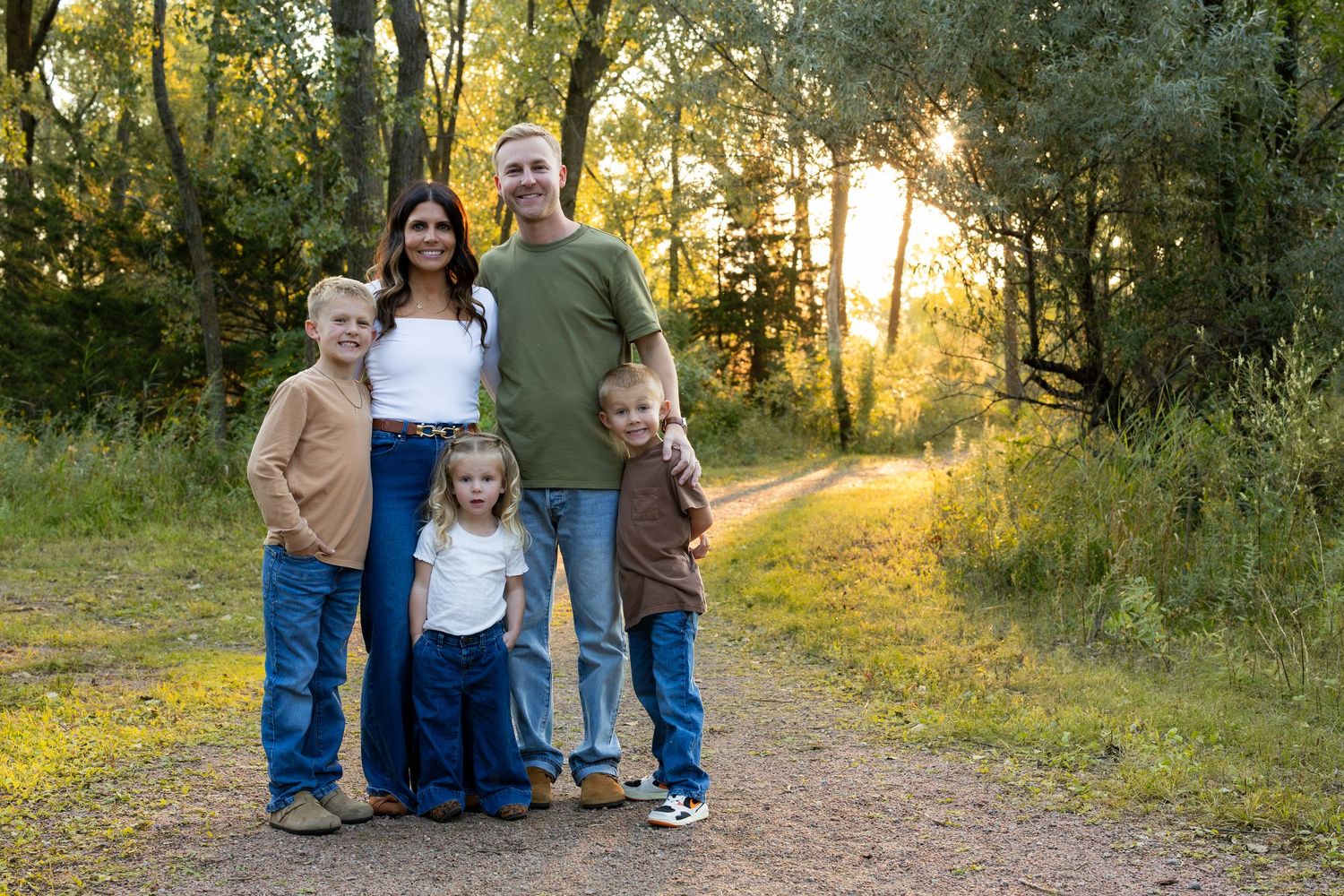 A group stands together on a sunlit forest path during golden hour as warm light filters through the trees.