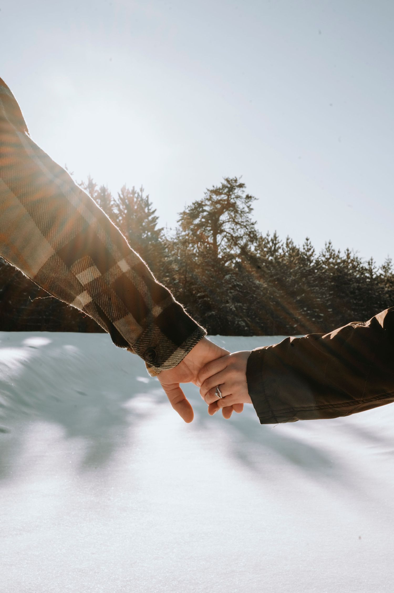 A couple holding hands in a snowy setting with the sun shining on them