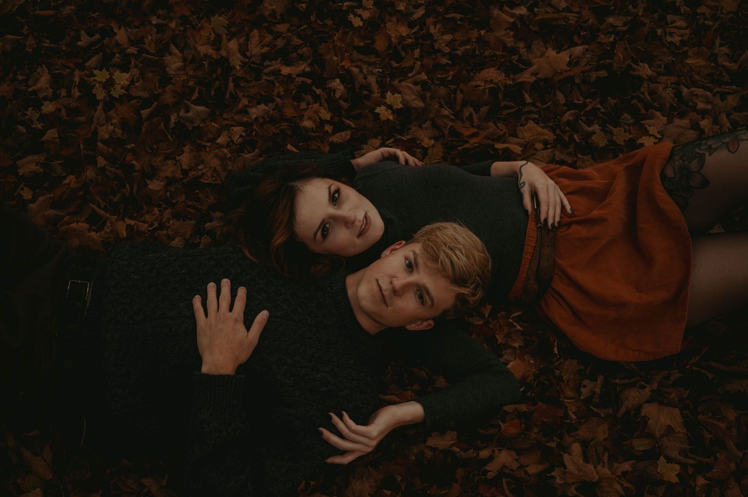 A couple lays down with their arms wrapped around each other on autumn leaves