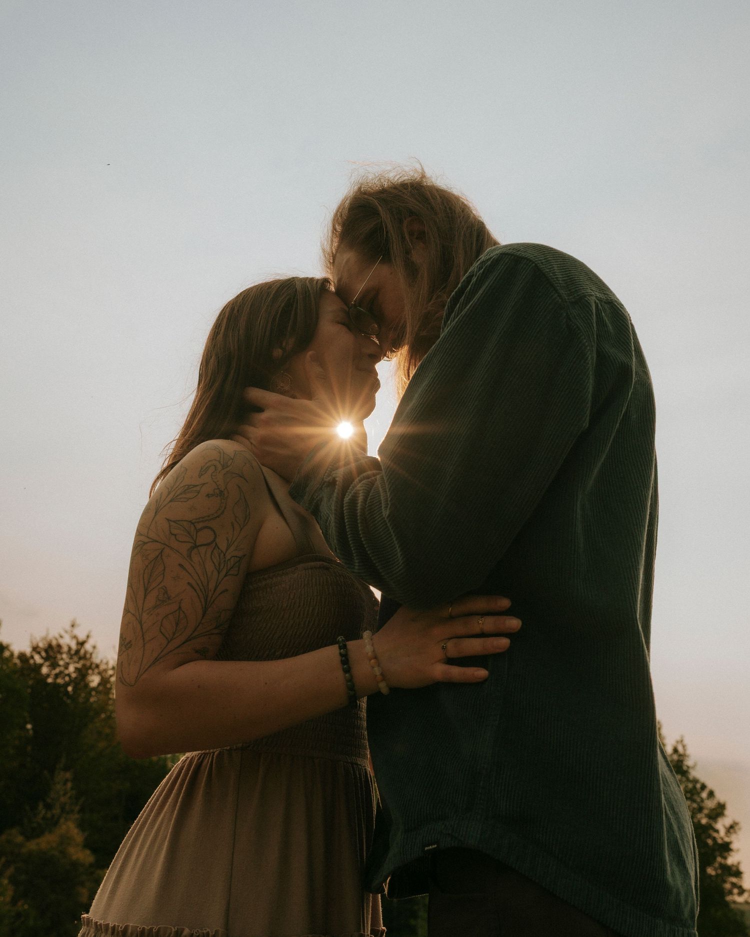 A couple touches foreheads with the sun peaking through between their noses