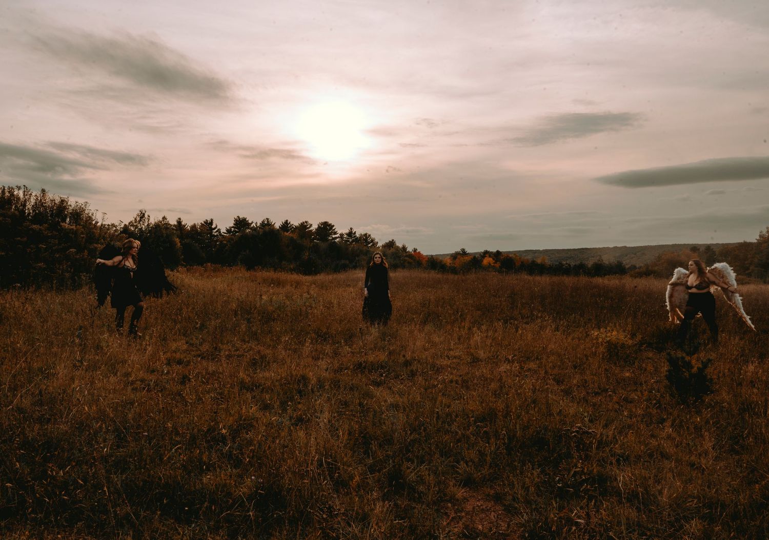 Halloween shoot in a field. 3 girls, 2 wearing wings and one facing the camera.