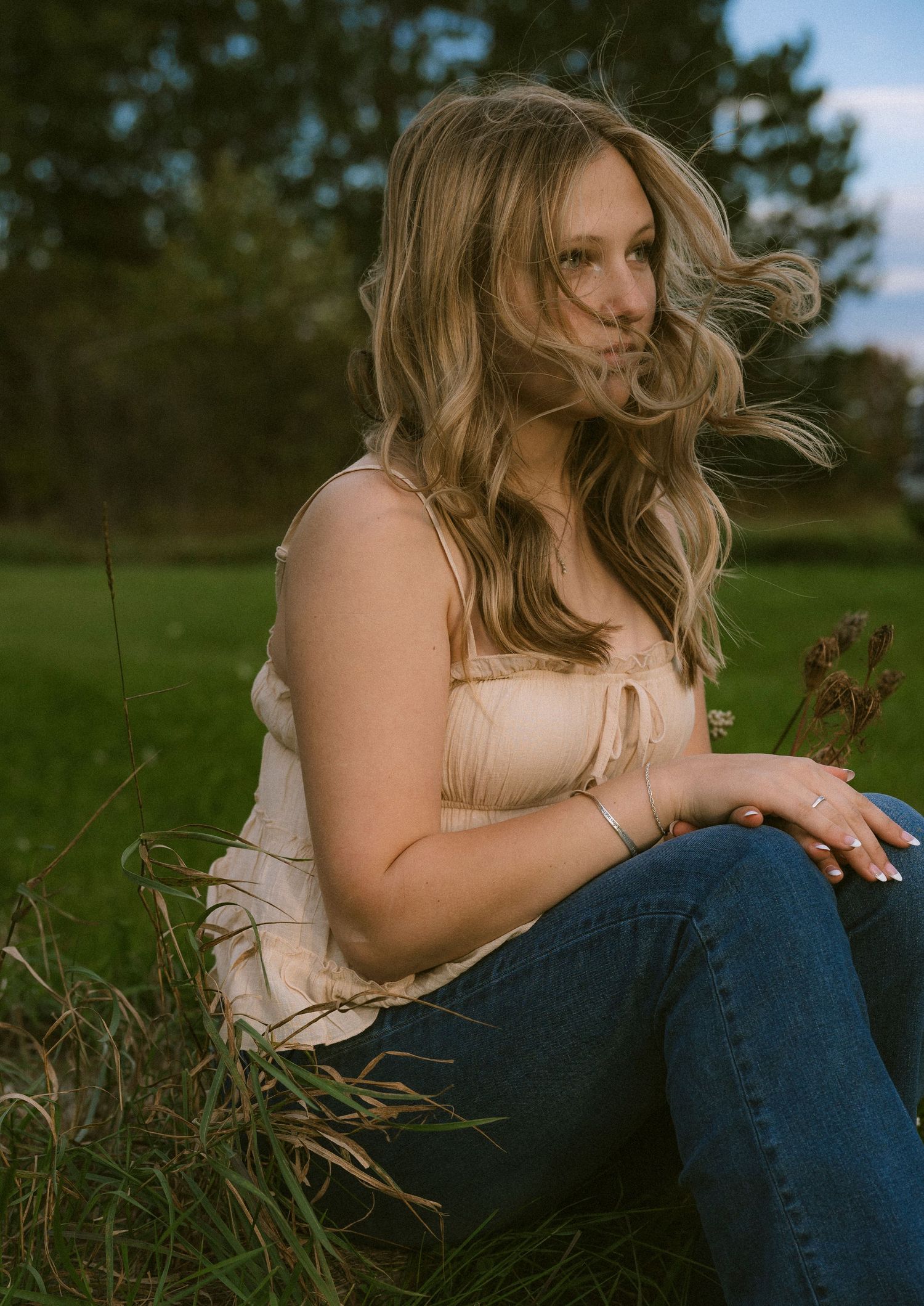 A high school senior sitting the green grass with the wind blowing though her hair