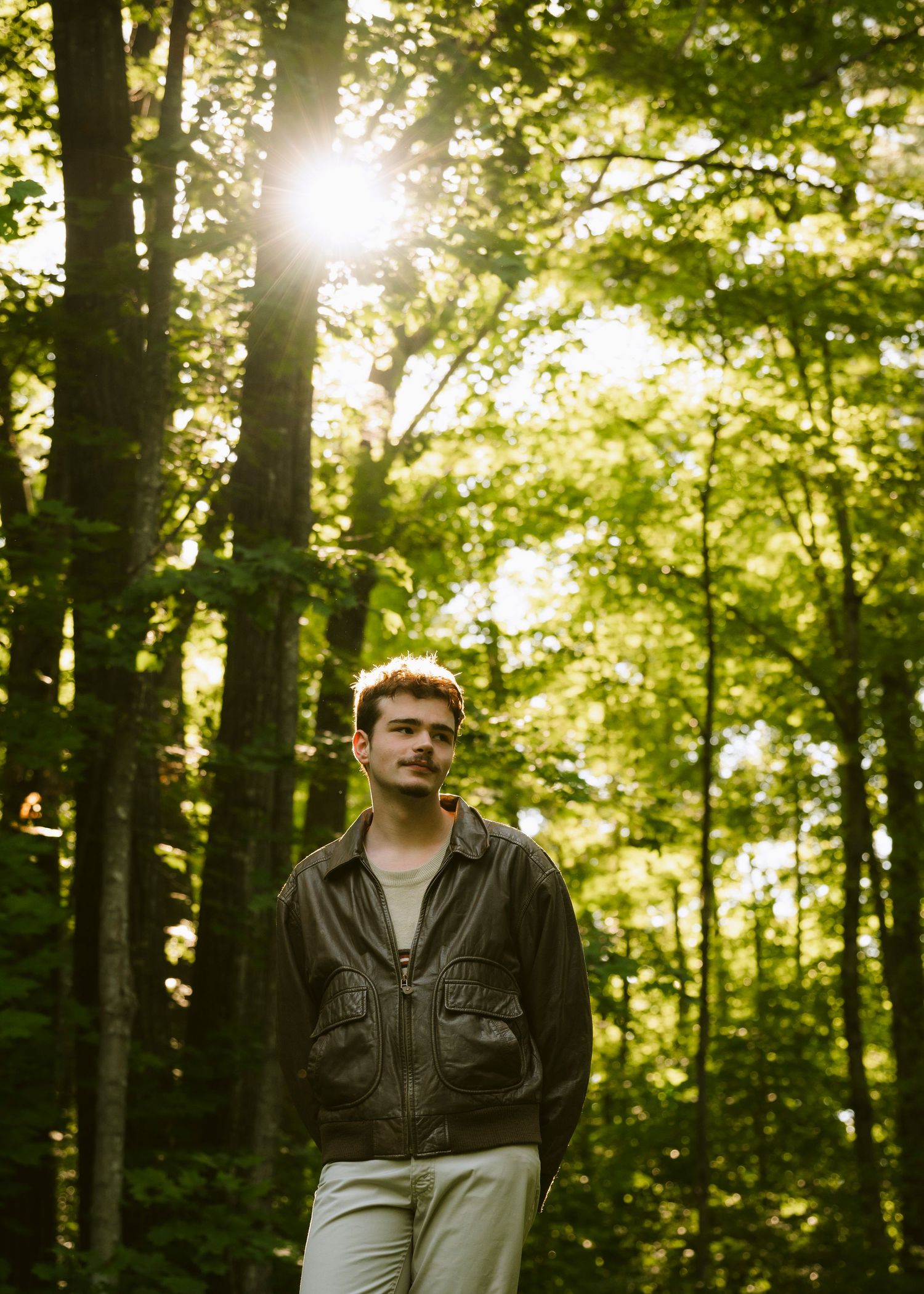A high school senior in a lush forest with the sun peaking through the canopy illuminating him