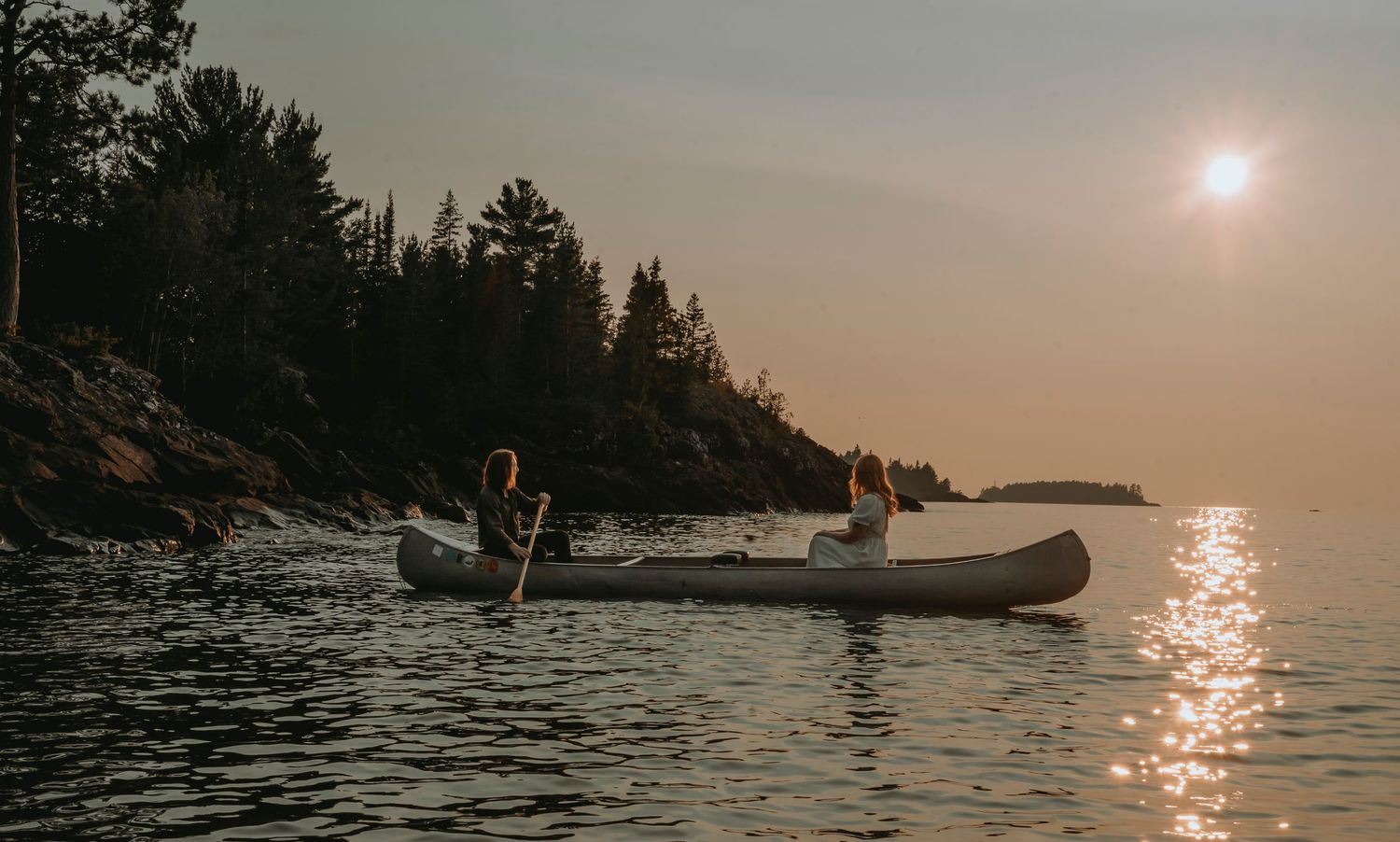 A couple in a canoe. paddling away from shore while the sun sets behind them