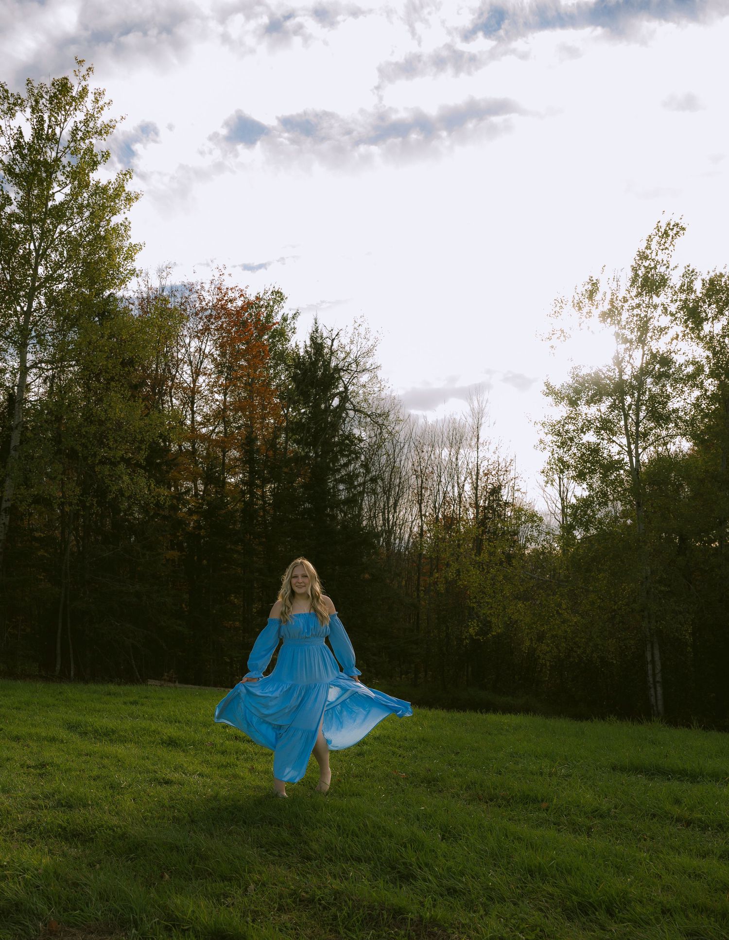 A high school senior in a blue flowing dress in a grass field
