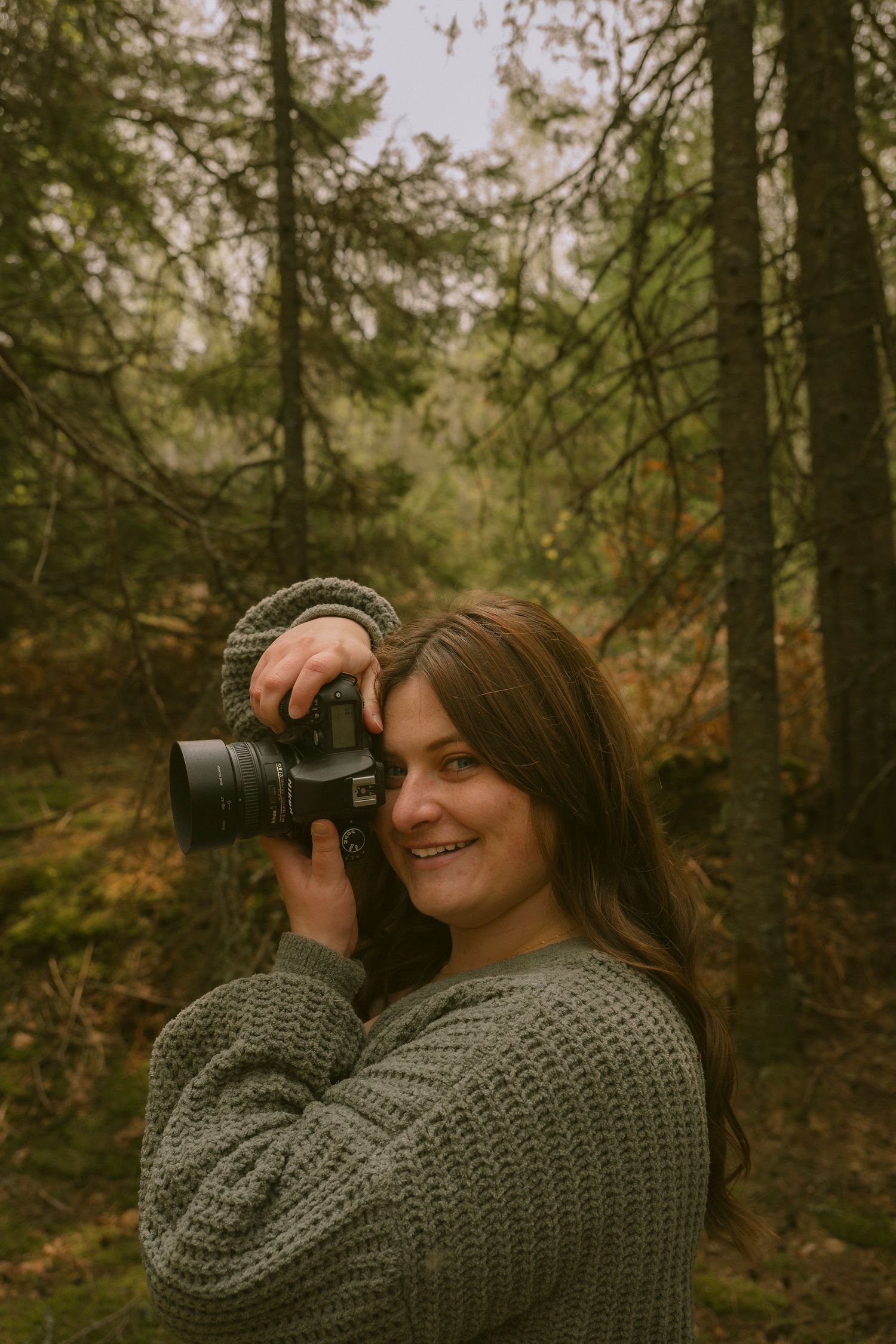 A woman holding a camera to her face in a cedar forest