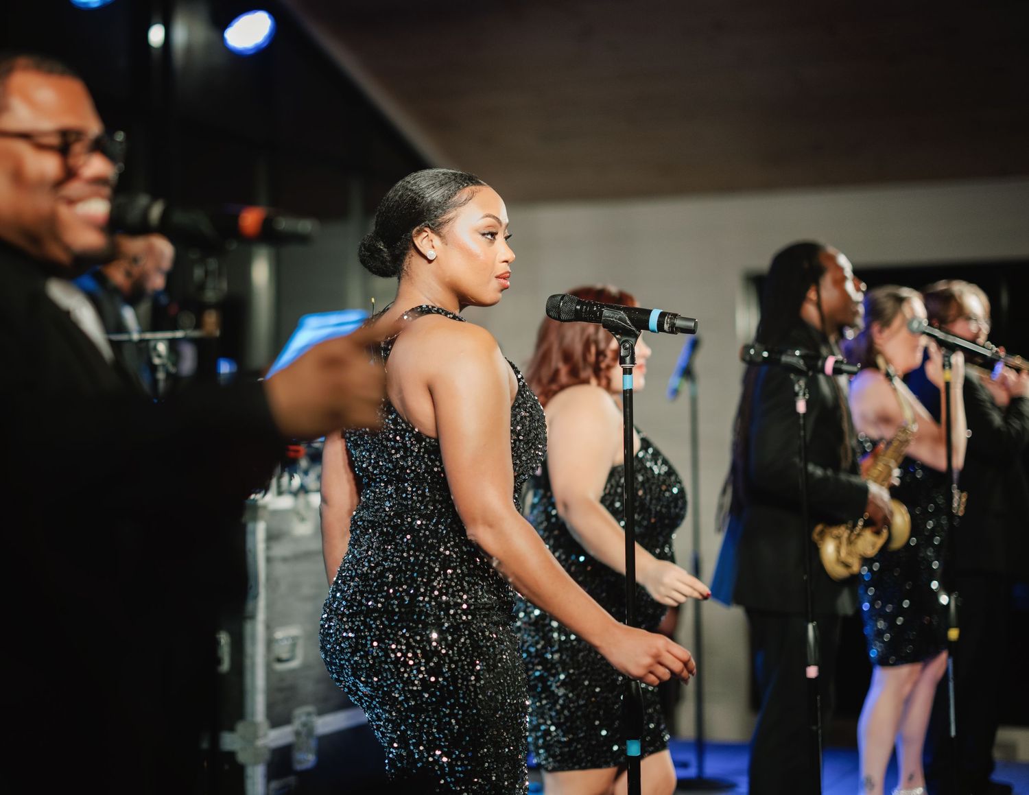 A group of performers in sparkly black outfits dance together on stage during a show.