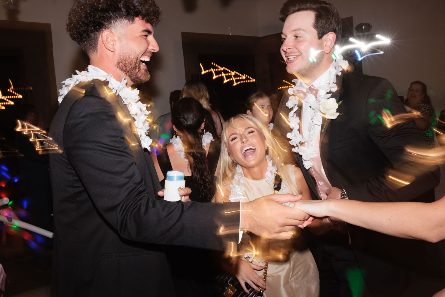 Wedding reception party scene with guests dancing and celebrating under festive lighting.