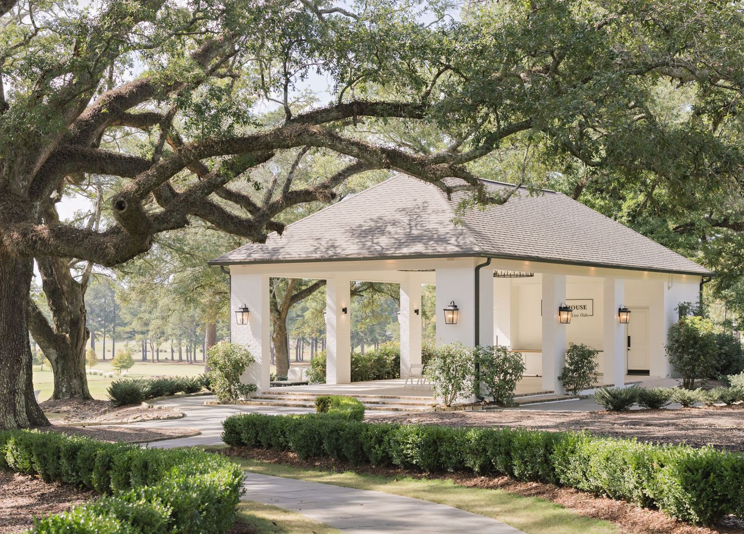 Tan ranch-style home with mature oak trees and landscaping along a curved driveway in a residential neighborhood.