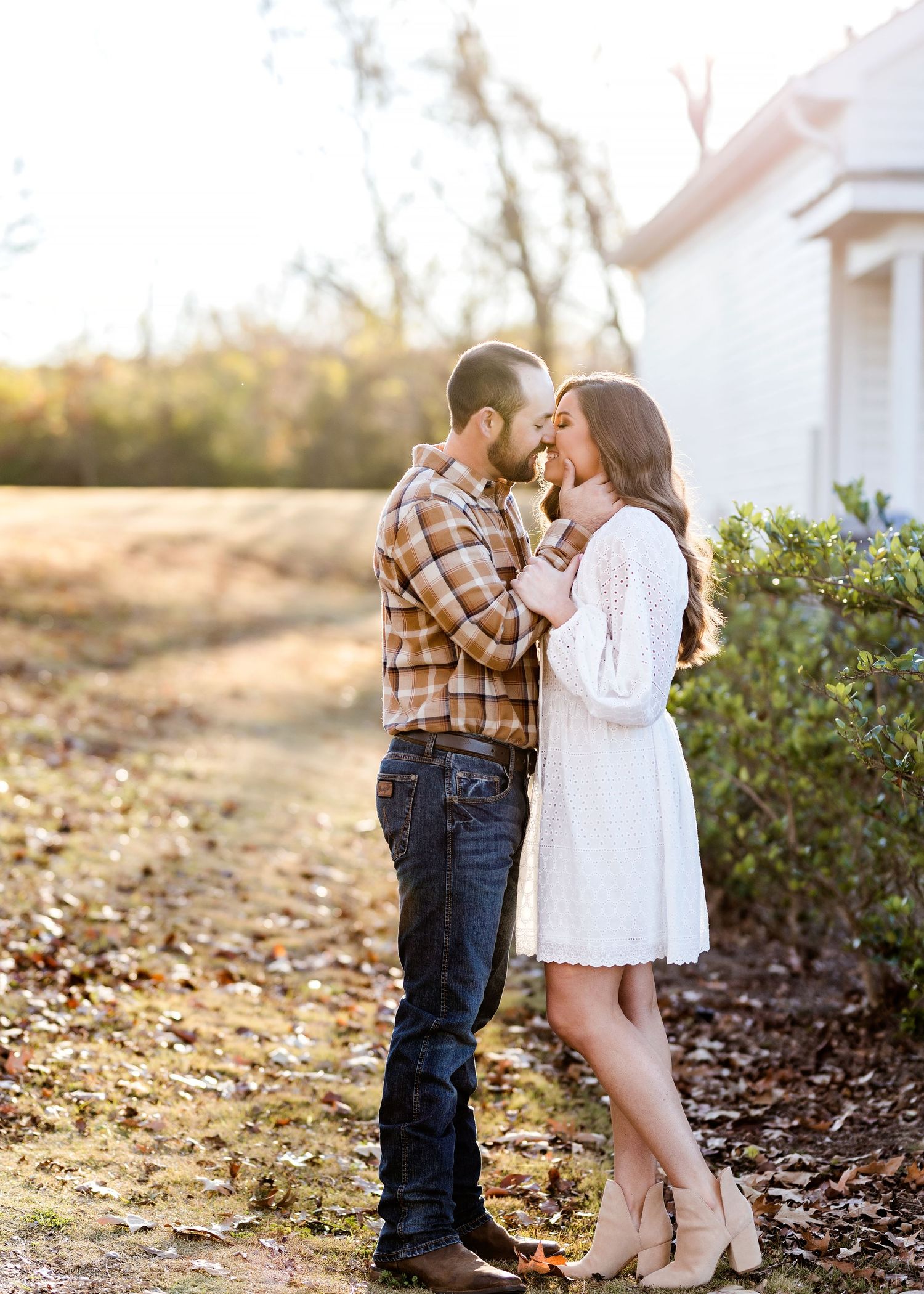 Couple in casual attire sharing intimate moments among fallen autumn leaves.