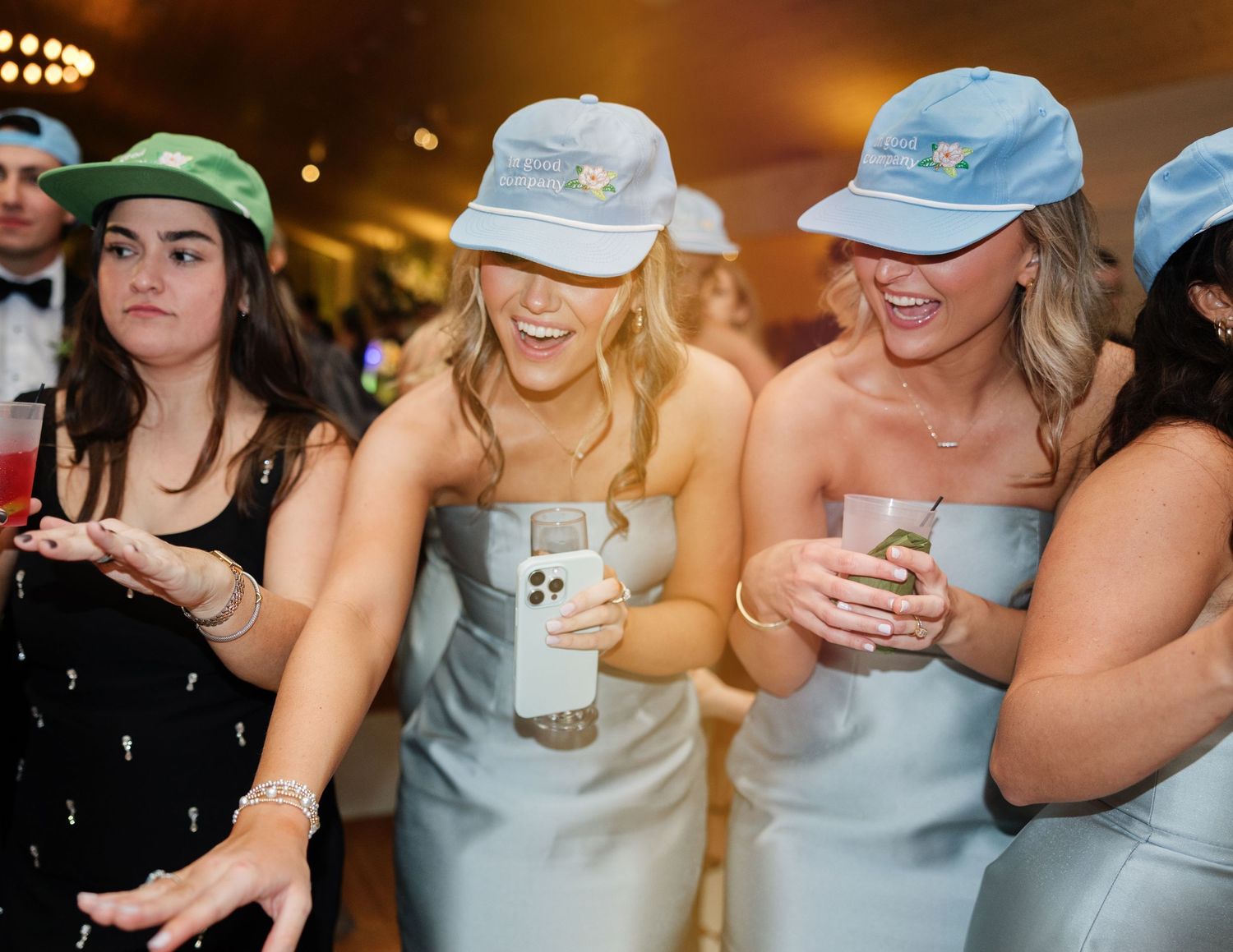 Wedding party members in matching blue dresses and caps check their phones during reception celebration.
