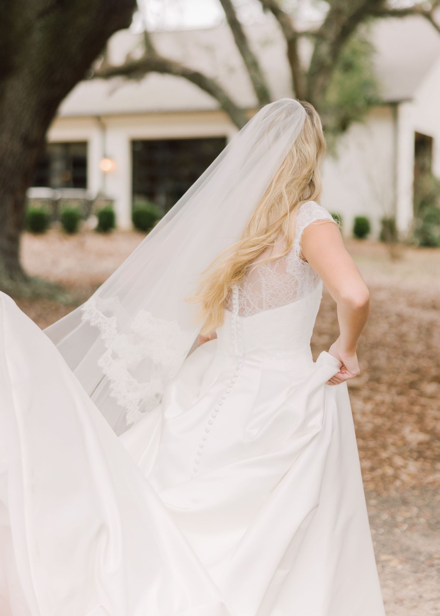 A bride in a flowing white wedding dress walks through a garden setting with her veil floating in the breeze.